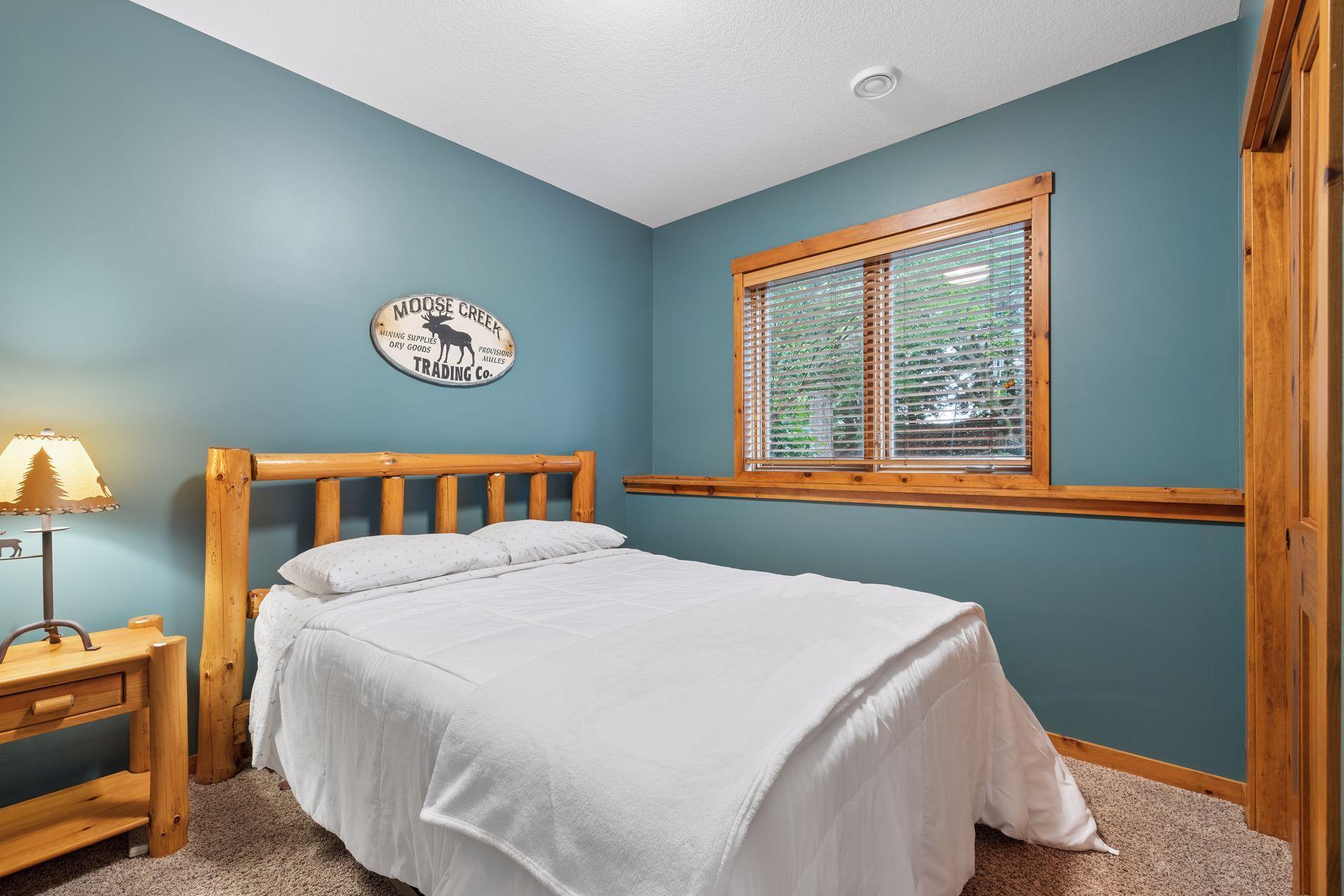 Bedroom with a log-style wooden bed, white bedding, teal walls, and a wood-trimmed window.