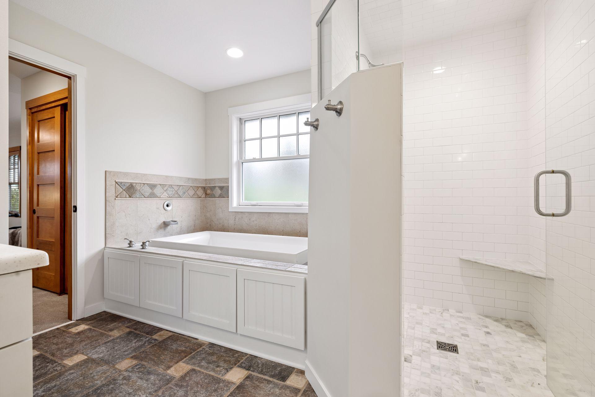 Bathroom with a built-in tub under a window and a separate white-tiled walk-in shower.
