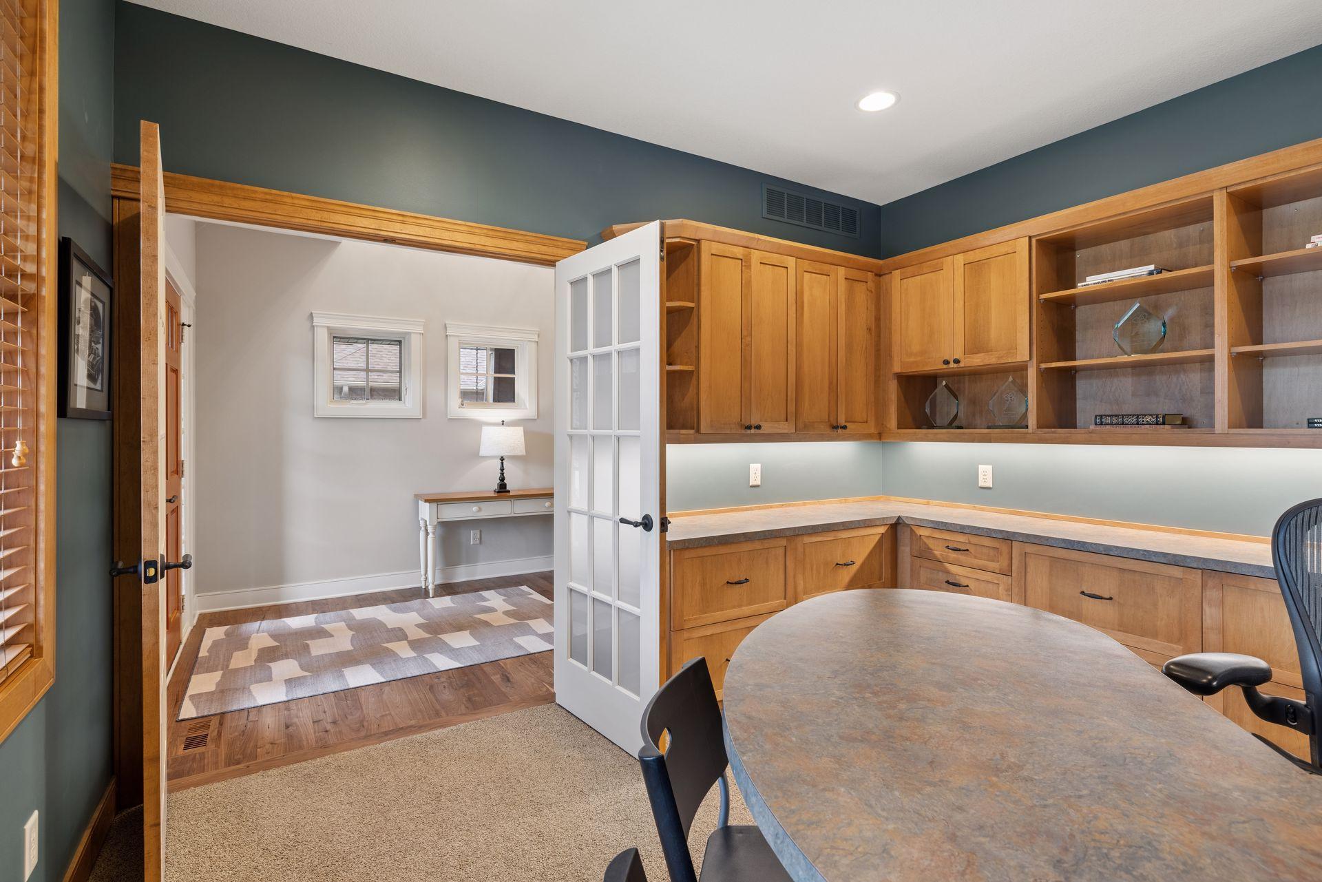 Home office with extensive wood cabinetry, open display shelves, and a large table.