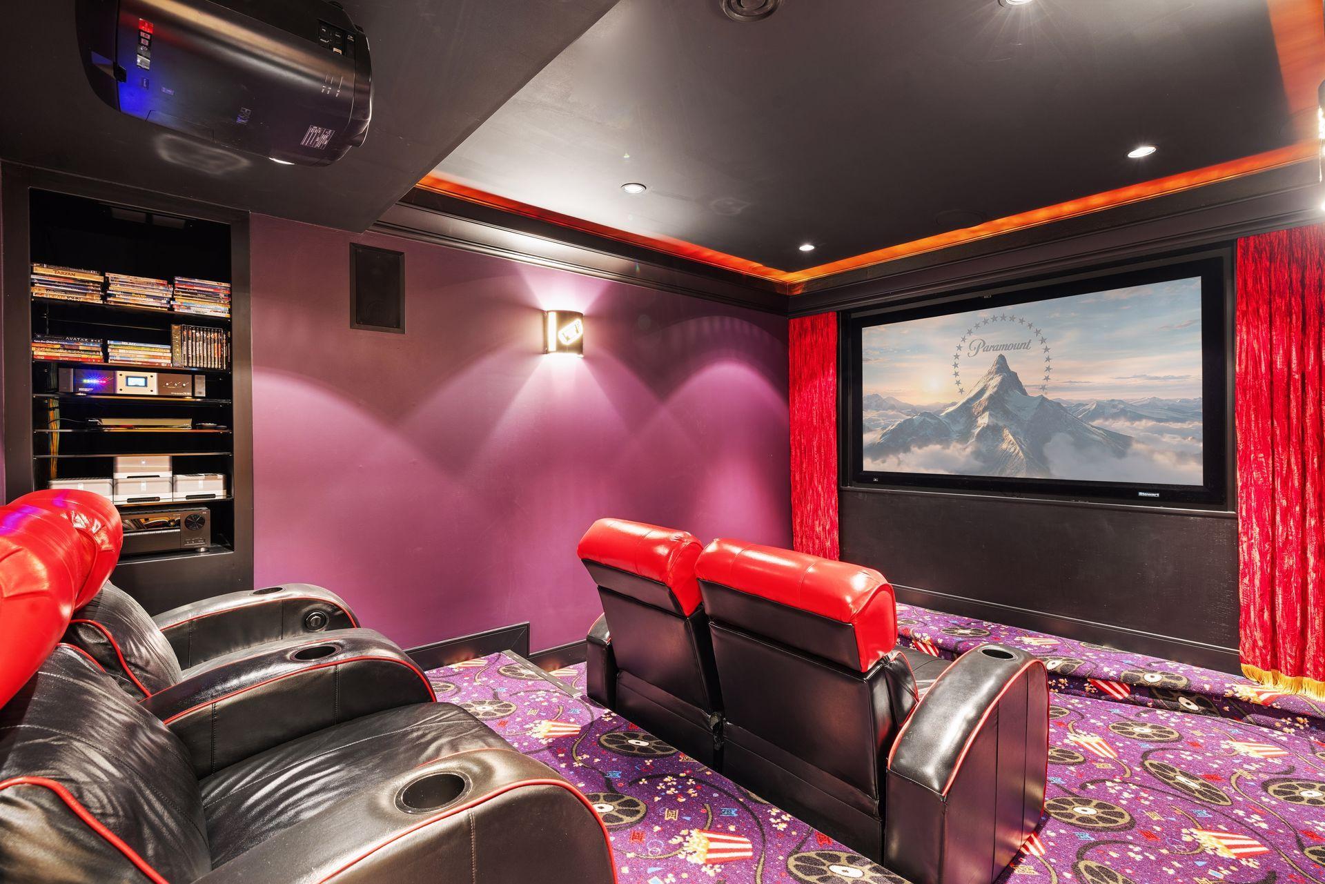 Home theater with red-and-black recliners, a large screen, red curtains, and colorful patterned carpet.