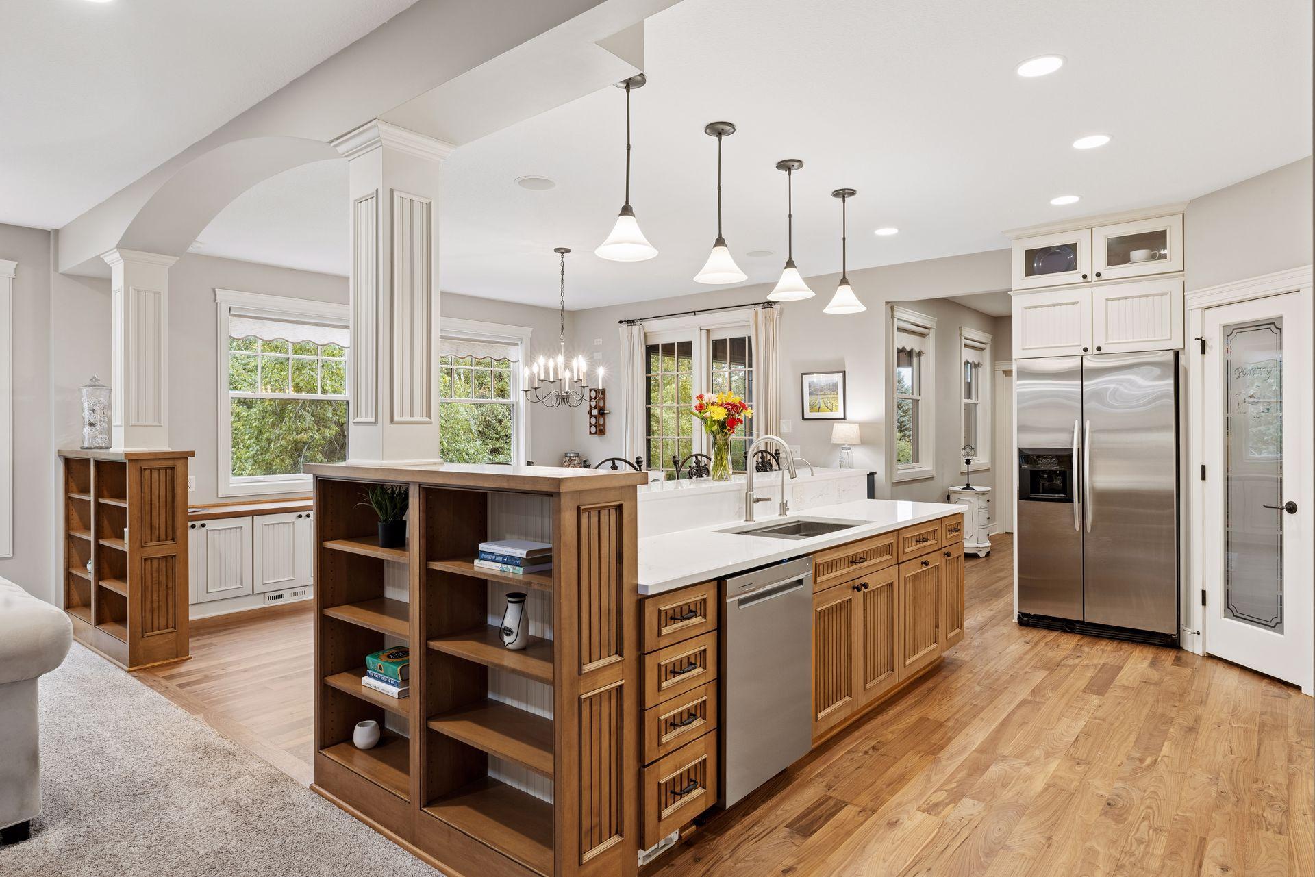 Bright kitchen with a large wood-cabinet island, white counters, stainless steel refrigerator, and hardwood floors.