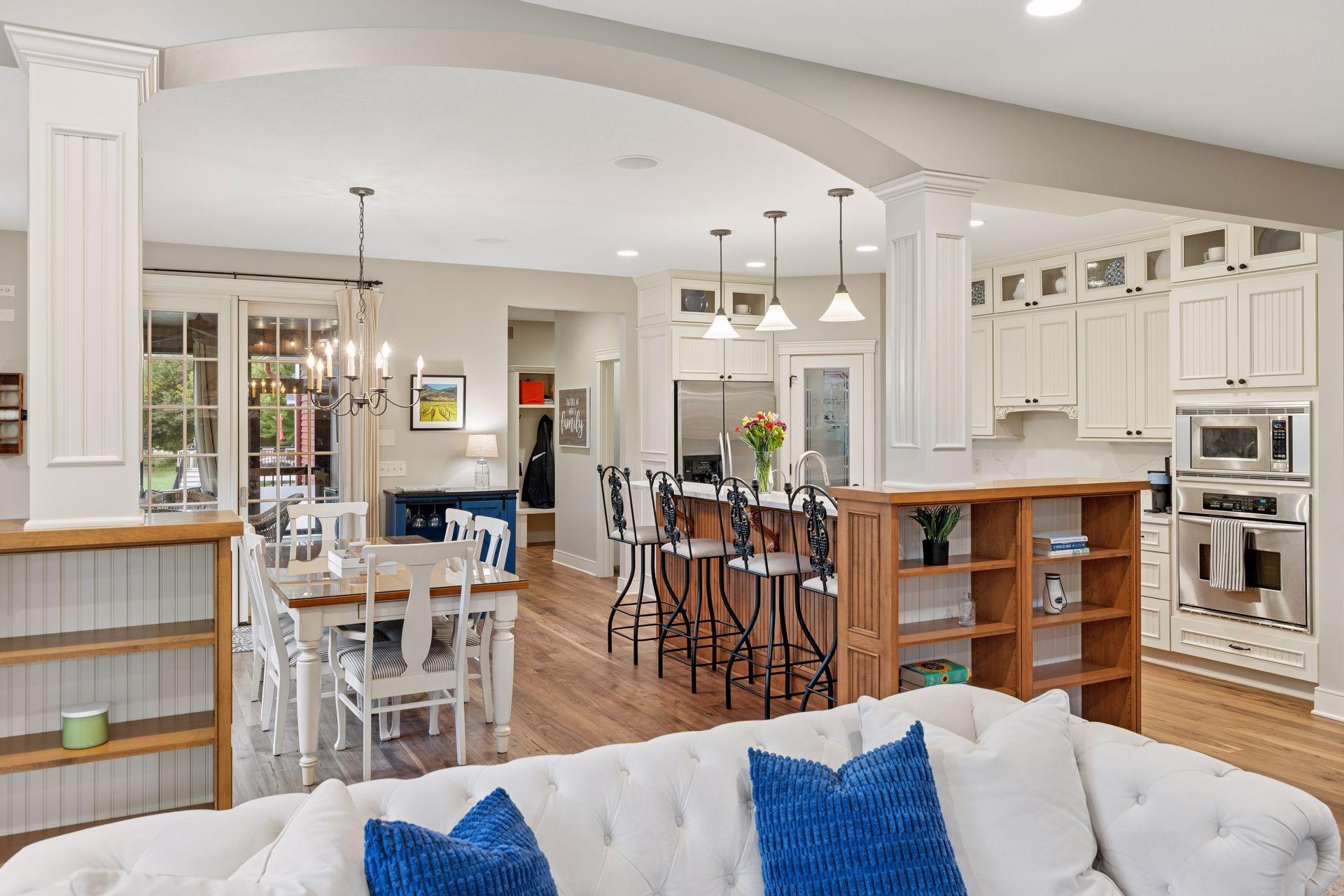 Open-plan kitchen and dining area with a wood island, white cabinetry, and a white sofa with blue pillows.