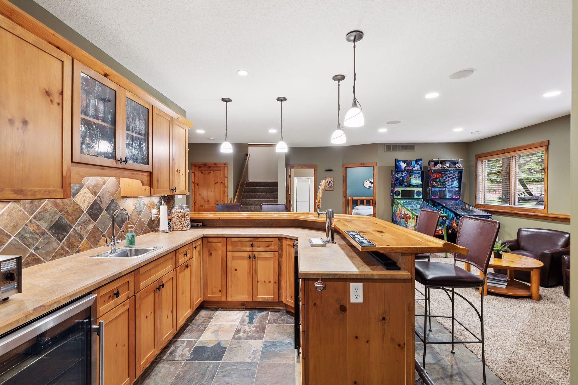 Kitchen with honey-toned wood cabinetry and a large island opening to a recreation area with pinball machines.