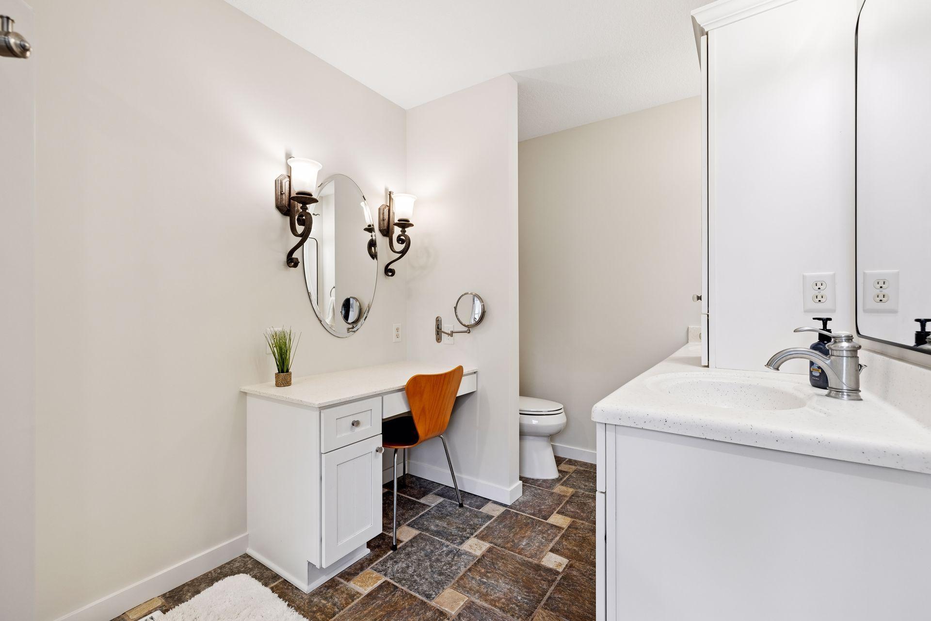 Bathroom with a makeup desk and orange chair beside the sink vanity and toilet.