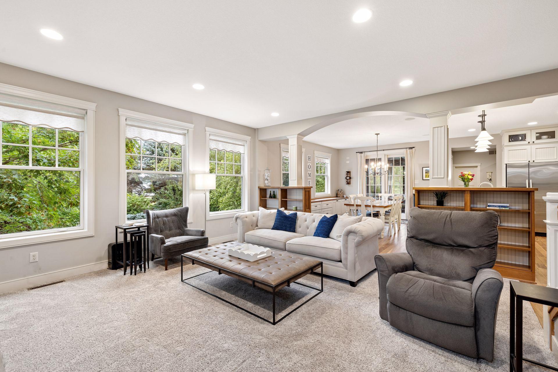 Furnished living room with a white sofa, gray armchairs, and an arched opening to the dining area and kitchen.