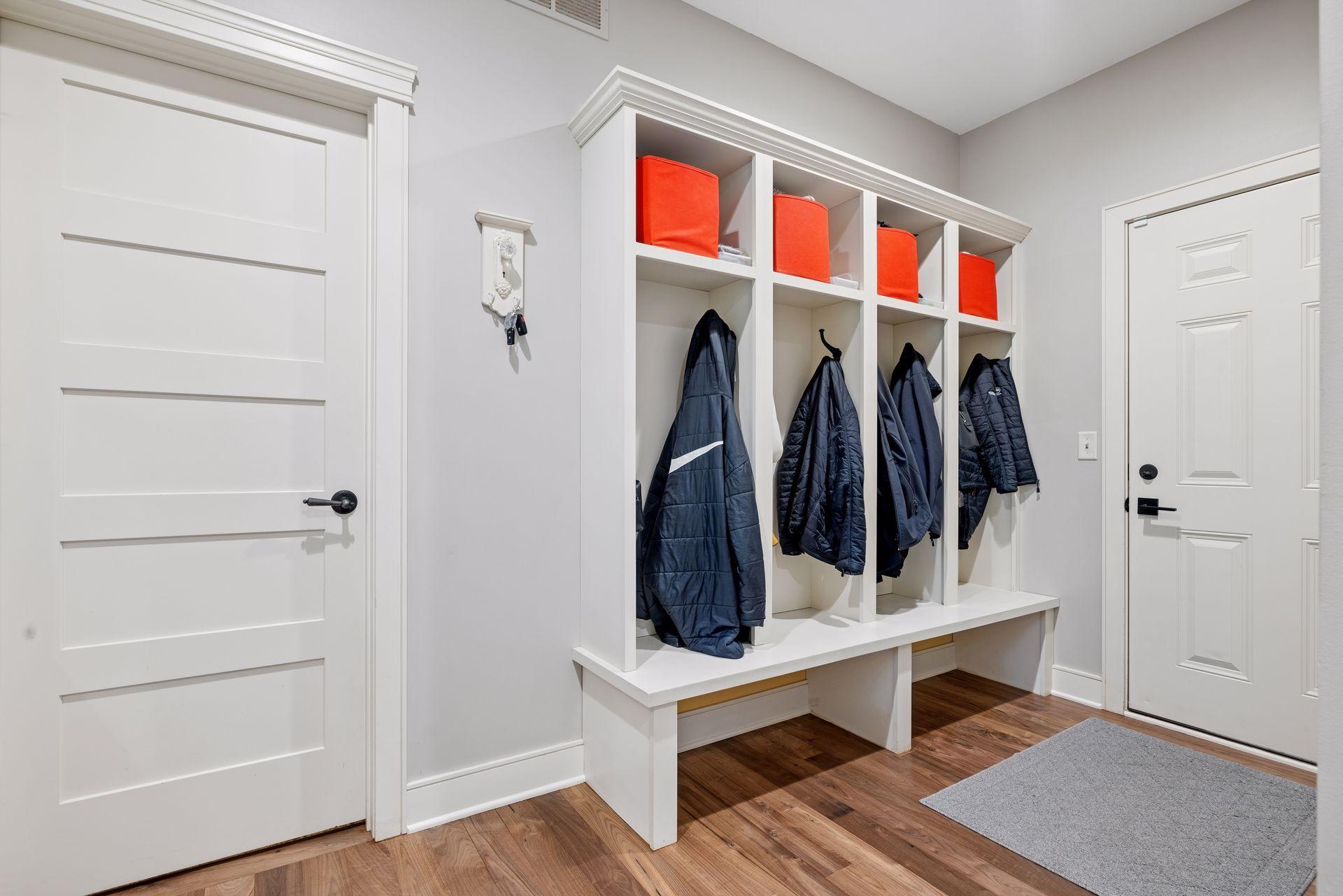Entryway with built-in coat cubbies, orange storage bins, a bench, and hardwood floors.