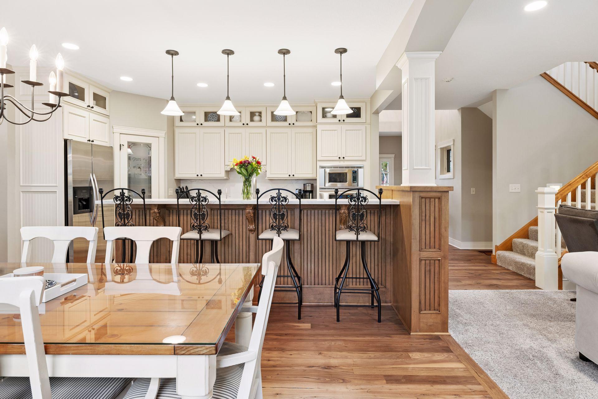 Open kitchen with white cabinets, a wood-paneled island, pendant lights, and an adjoining dining table.