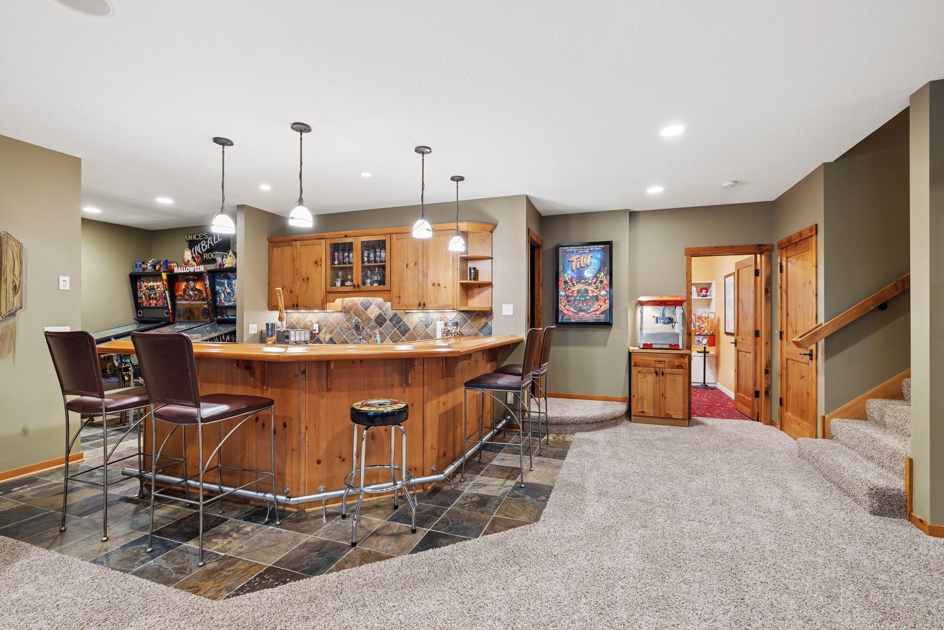 Basement recreation room with a wooden bar, pinball machines, popcorn maker, and carpeted staircase.
