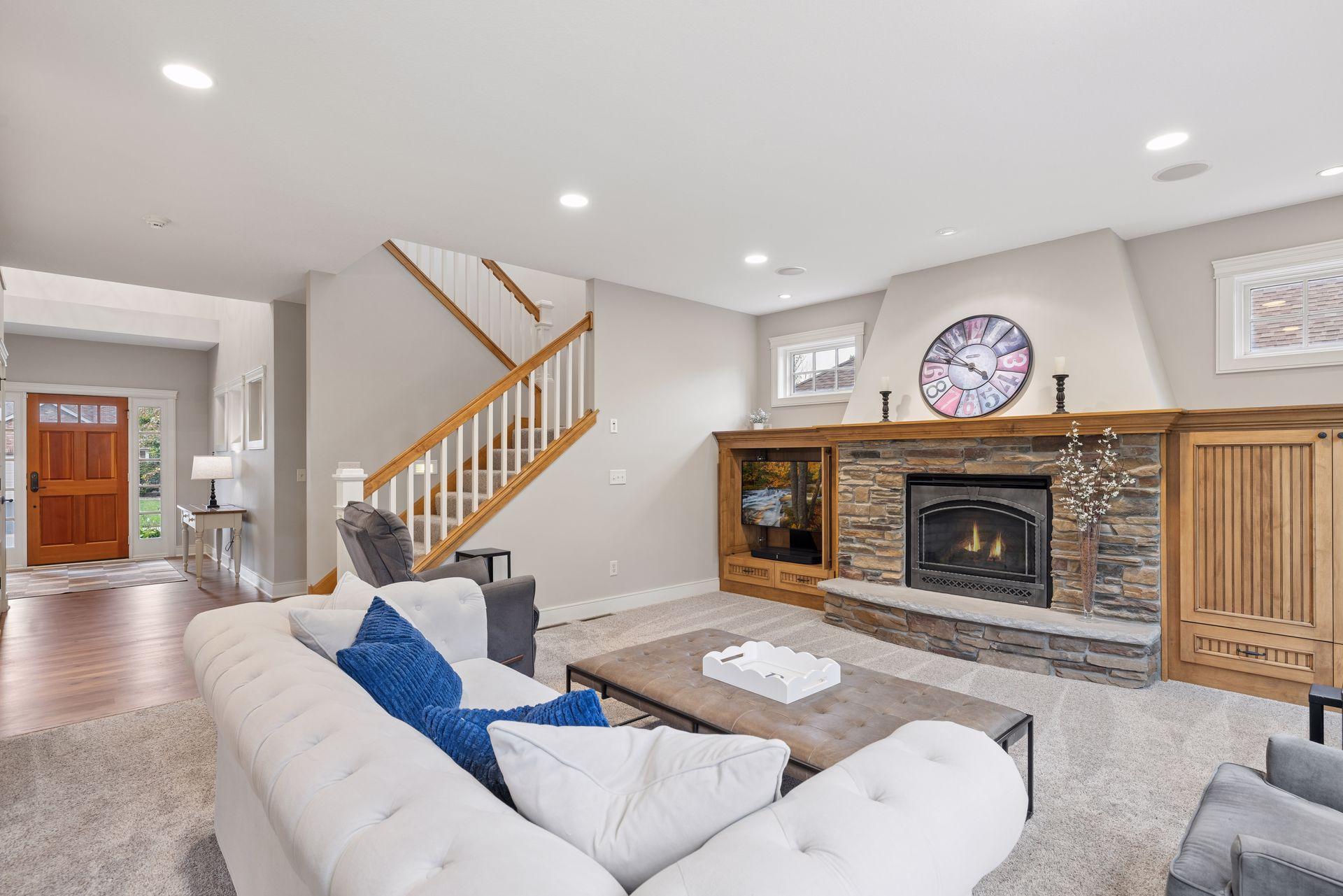 Furnished living room with a stone fireplace, wood built-ins, and a staircase.