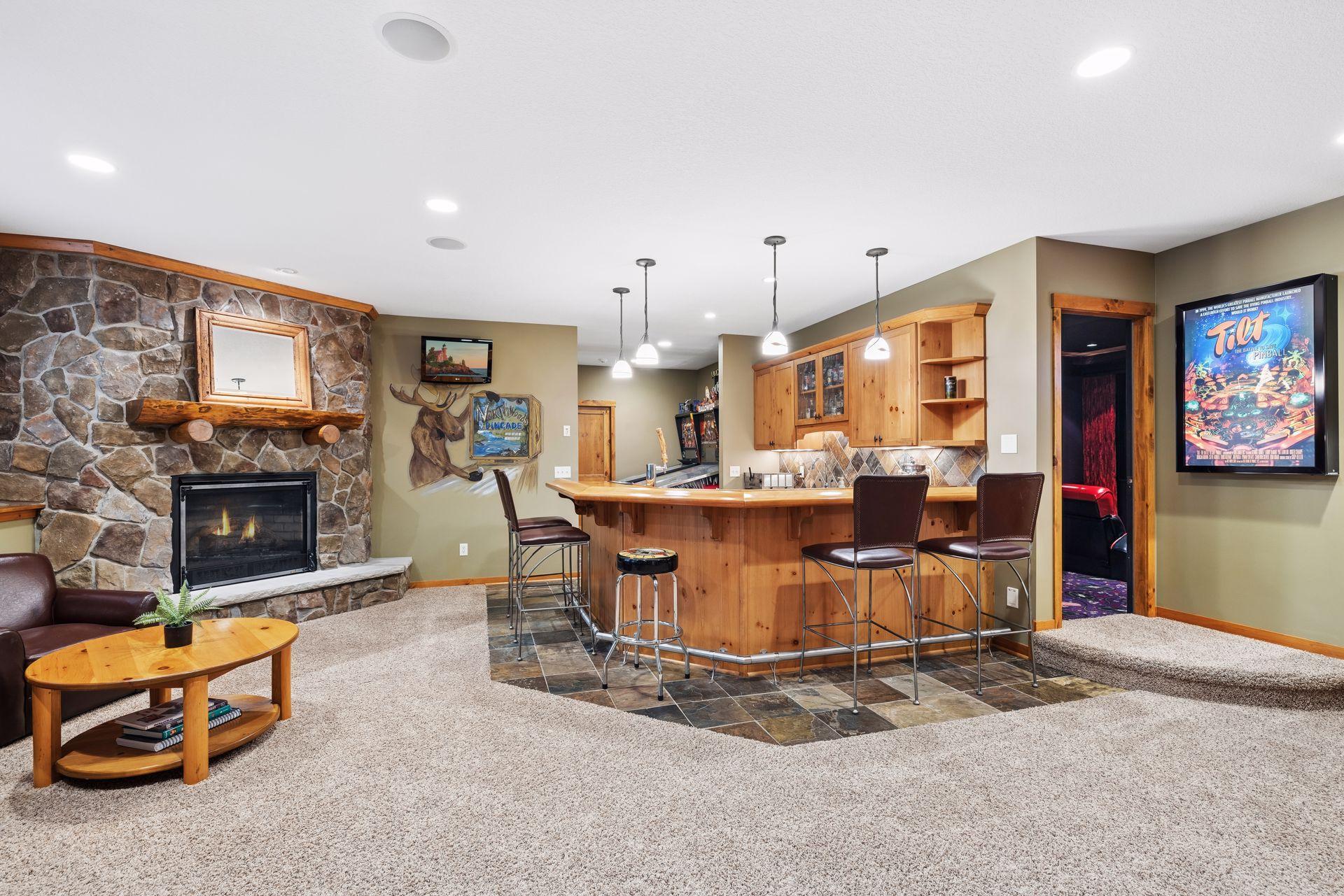 Basement recreation room with a curved wood bar, stone fireplace, and arcade room doorway.