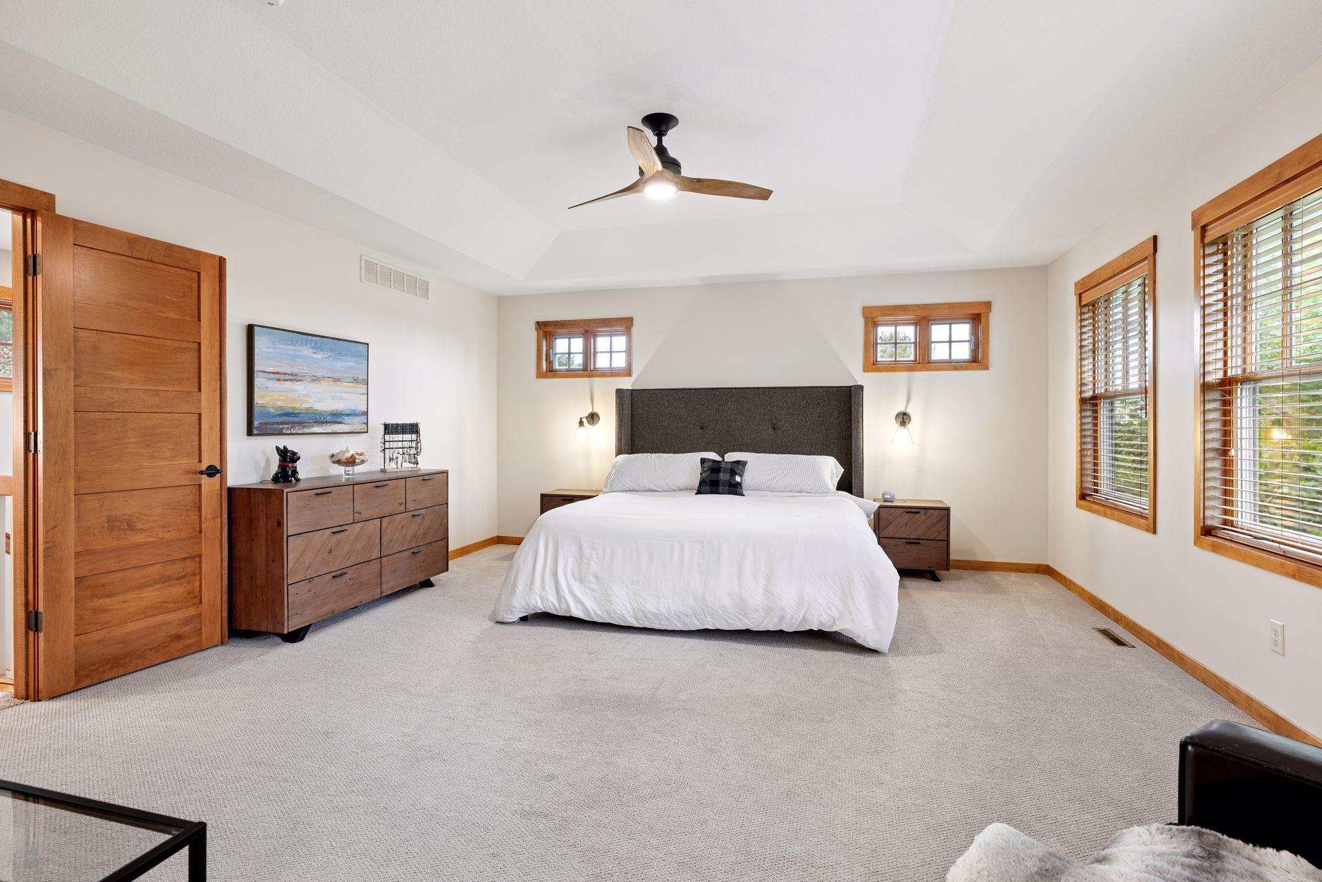 Bedroom with a king bed, charcoal headboard, warm wood trim, and windows with wood blinds.