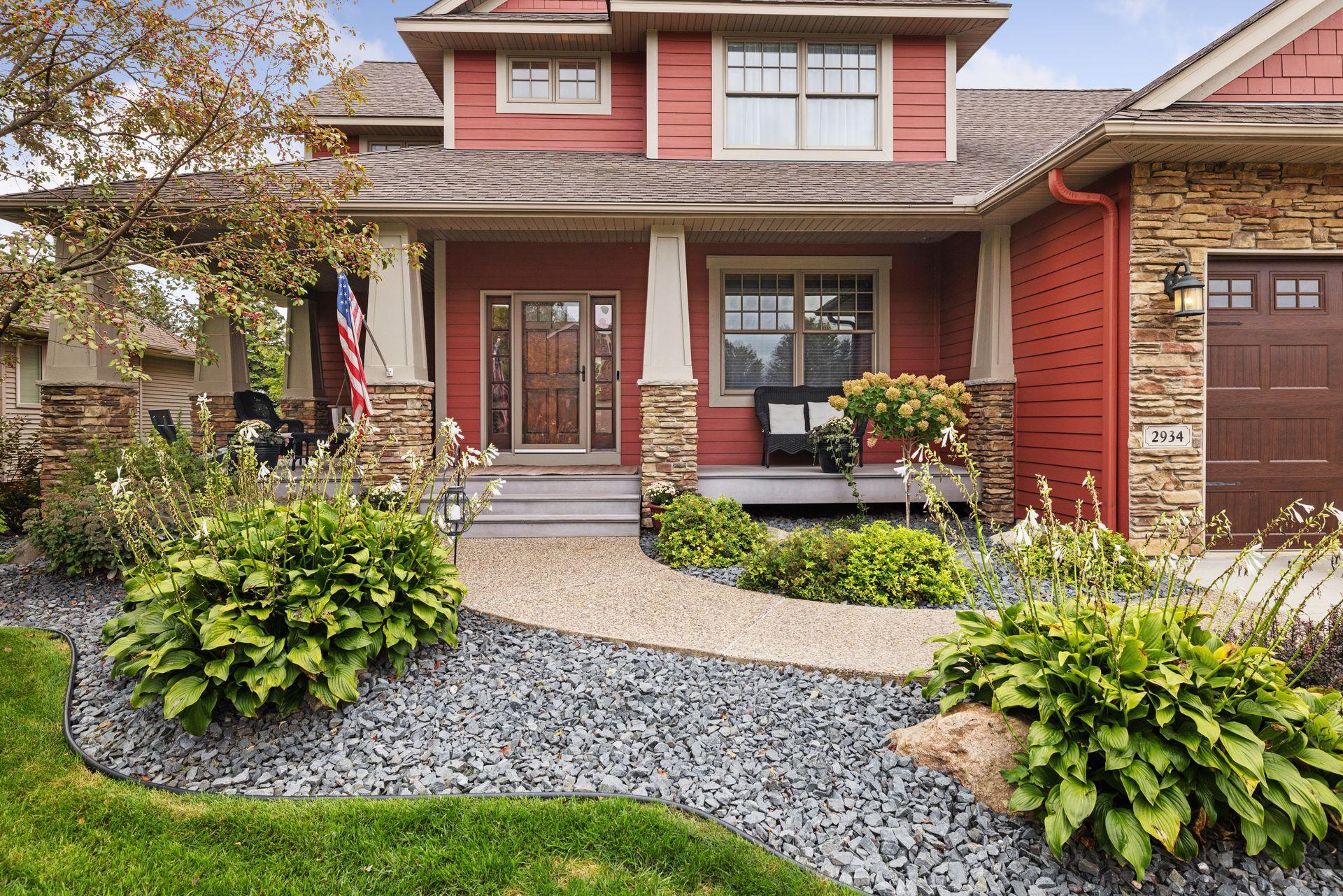 Red two-story home with a stone-accented porch and landscaped rock garden.