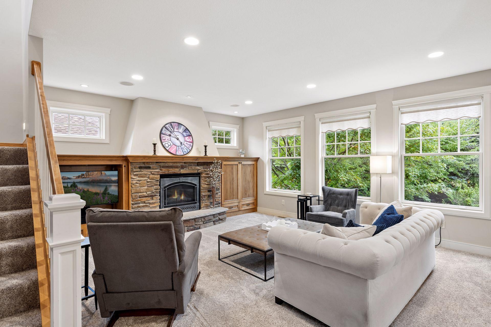 Living room with a stone fireplace, built-in cabinetry, and large windows overlooking greenery.