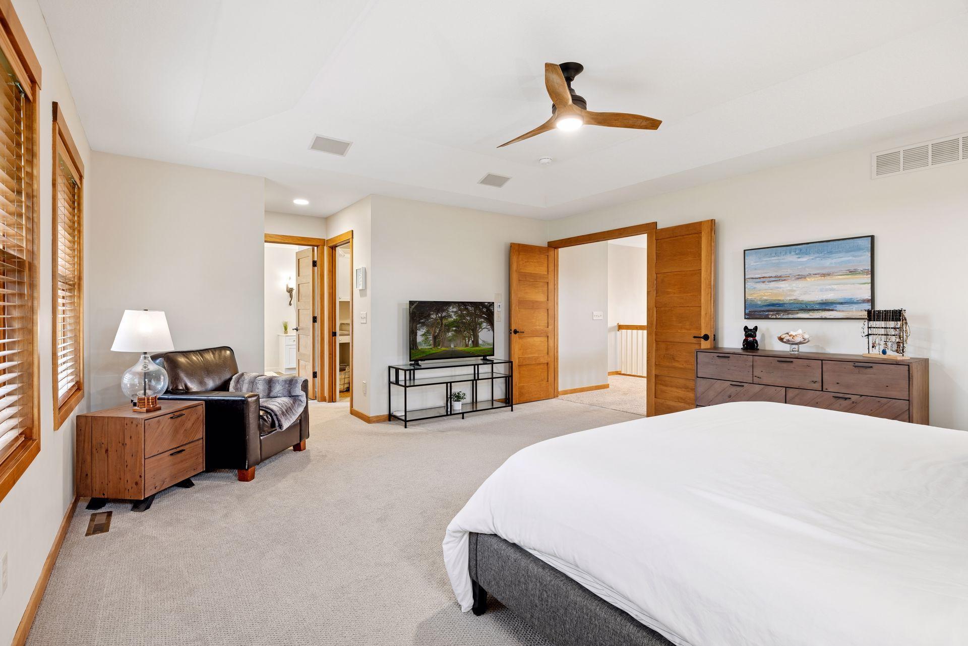 Furnished bedroom with a large bed, wood-trimmed doors, and a sitting area by the windows.