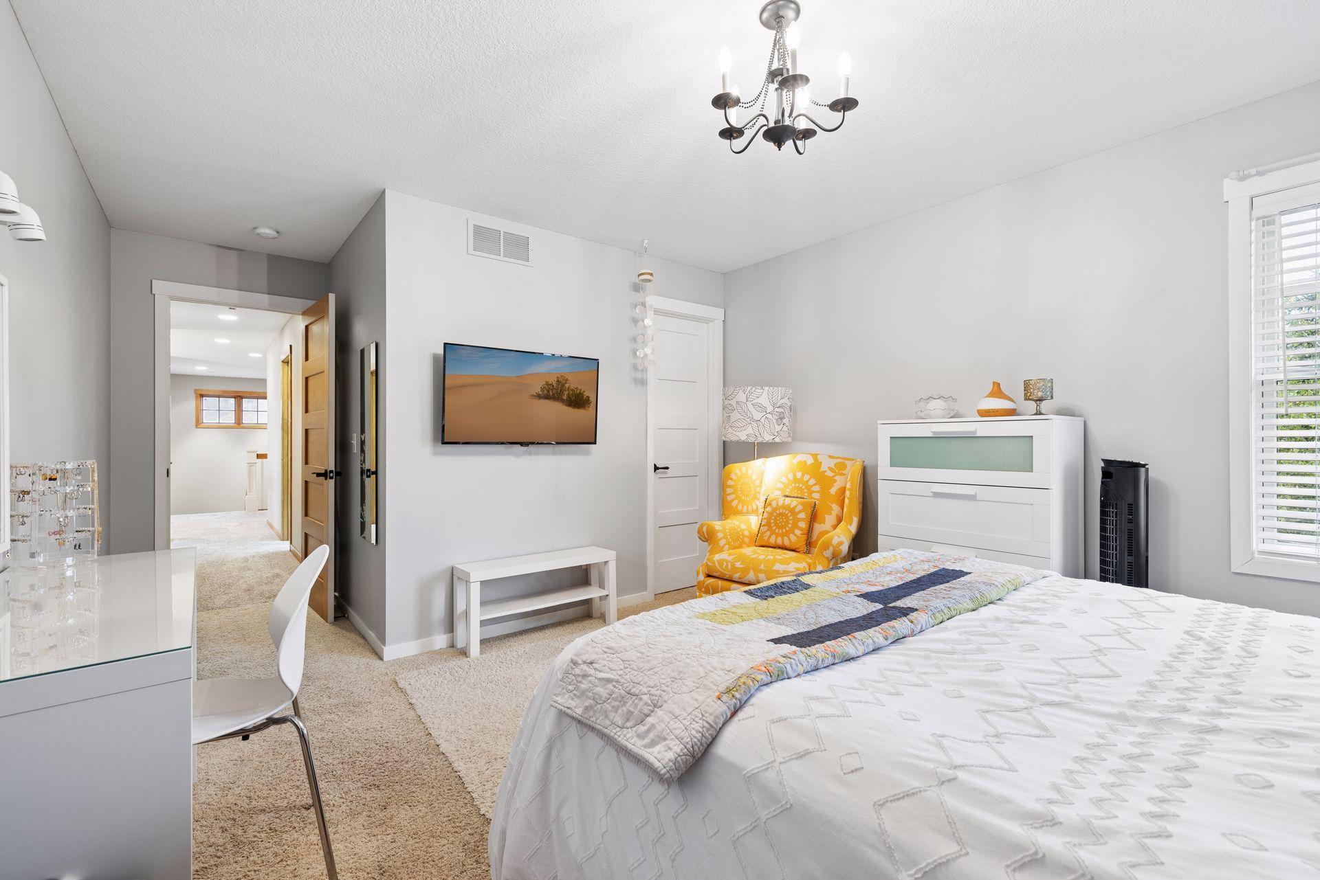 Furnished bedroom with a large white bed, yellow floral armchair, and wall-mounted television.