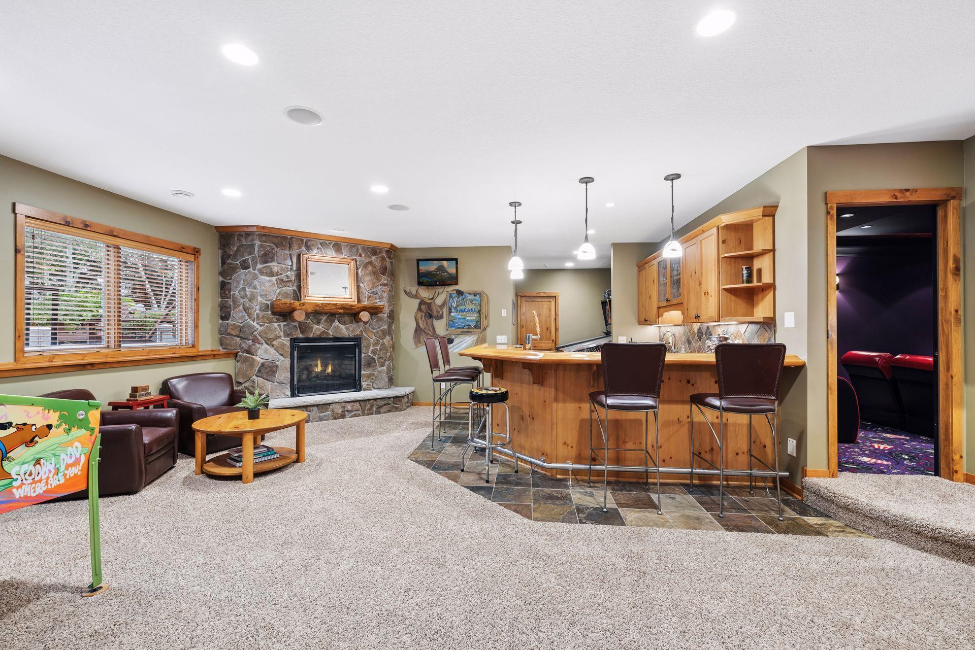 Recreation room with a stone fireplace, wood bar, and doorway to a home theater.