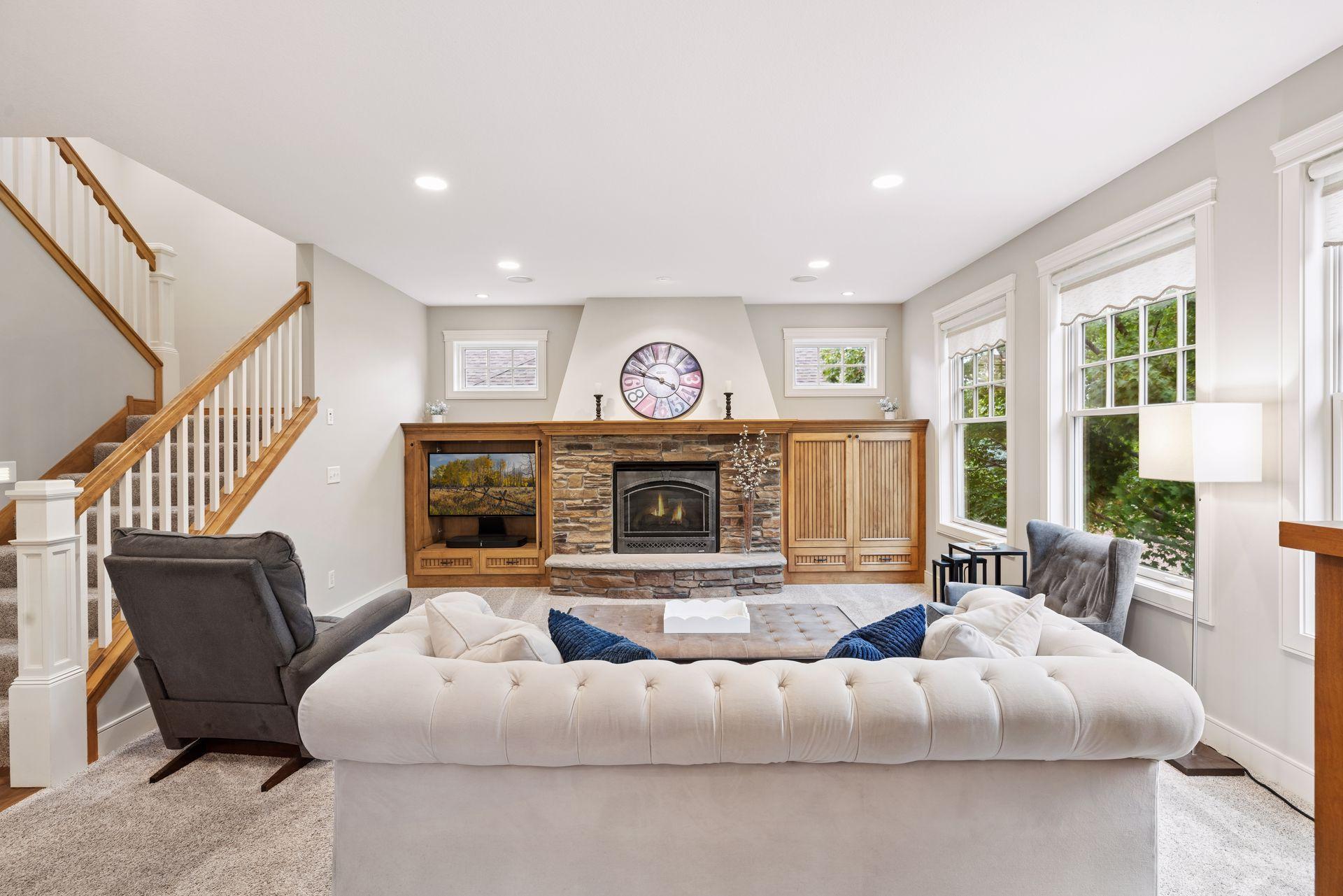 Living room with a stone fireplace, wood built-ins, staircase, and tall windows.