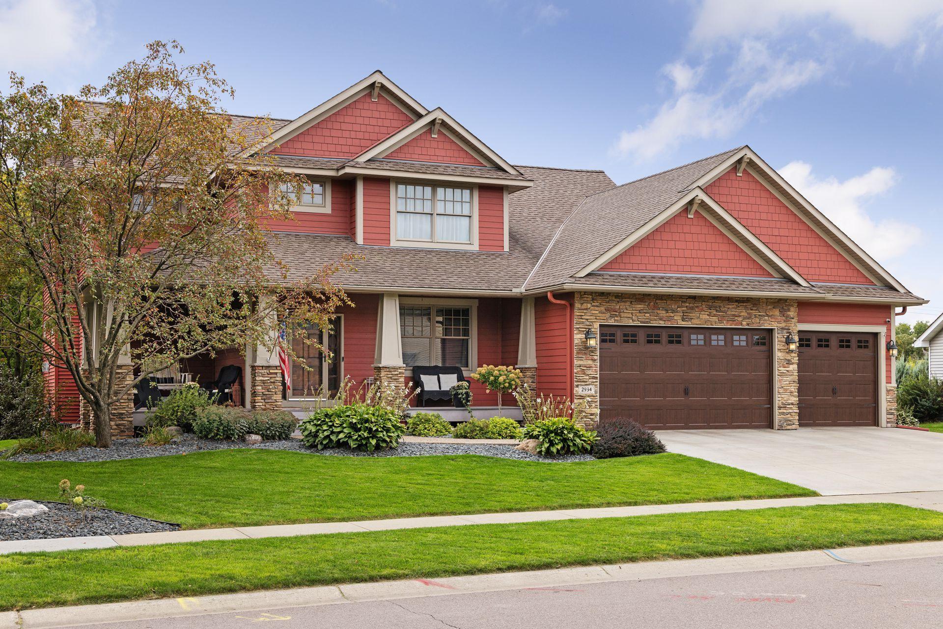 Red two-story home with stone accents, a covered porch, and a two-door garage.