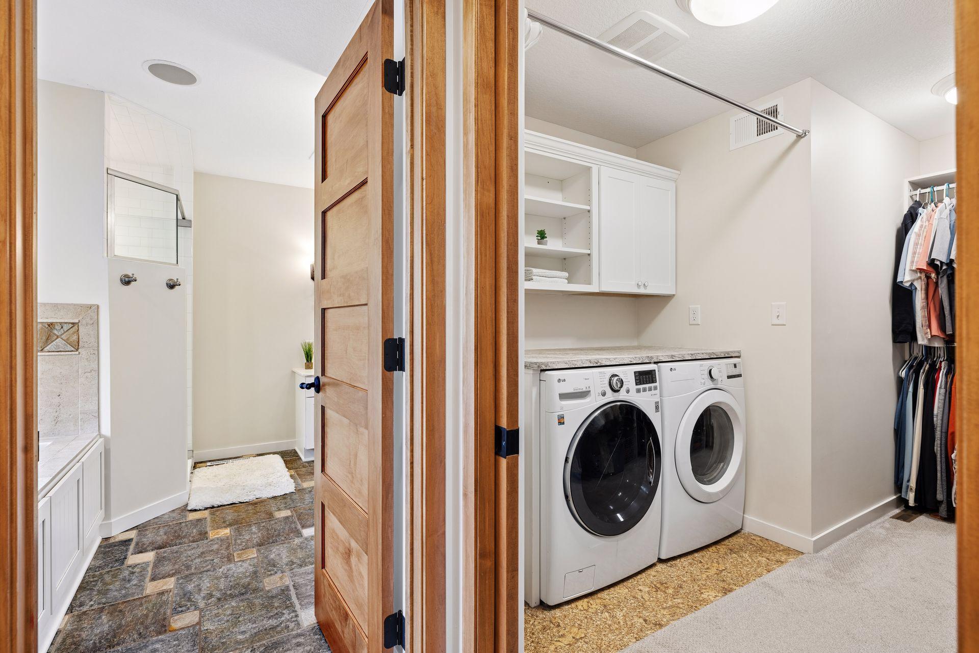Laundry room with front-loading washer and dryer, built-in cabinets, and adjoining tiled bathroom.