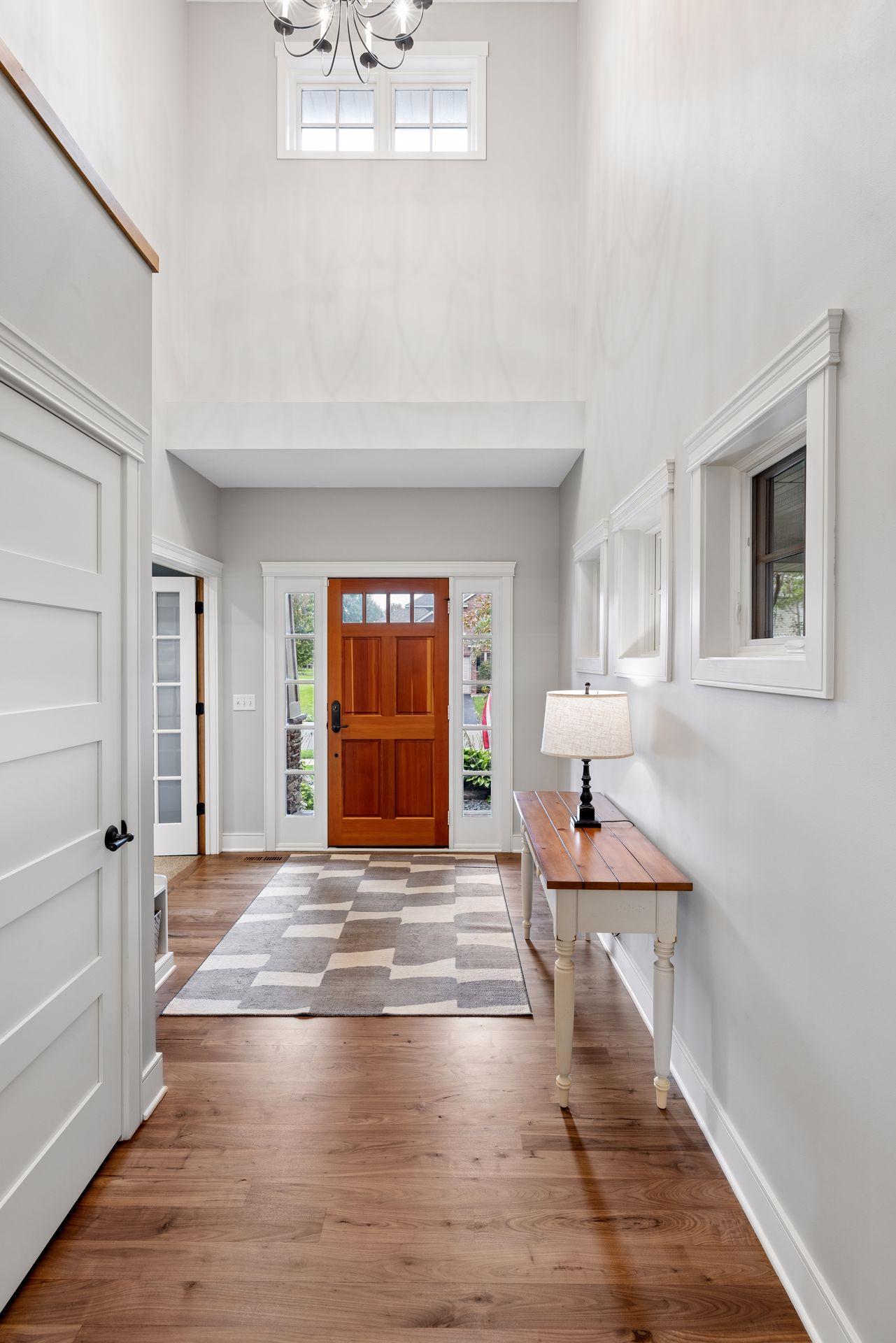 Double-height entry foyer with a wood front door, hardwood floors, and a console table beneath the windows.