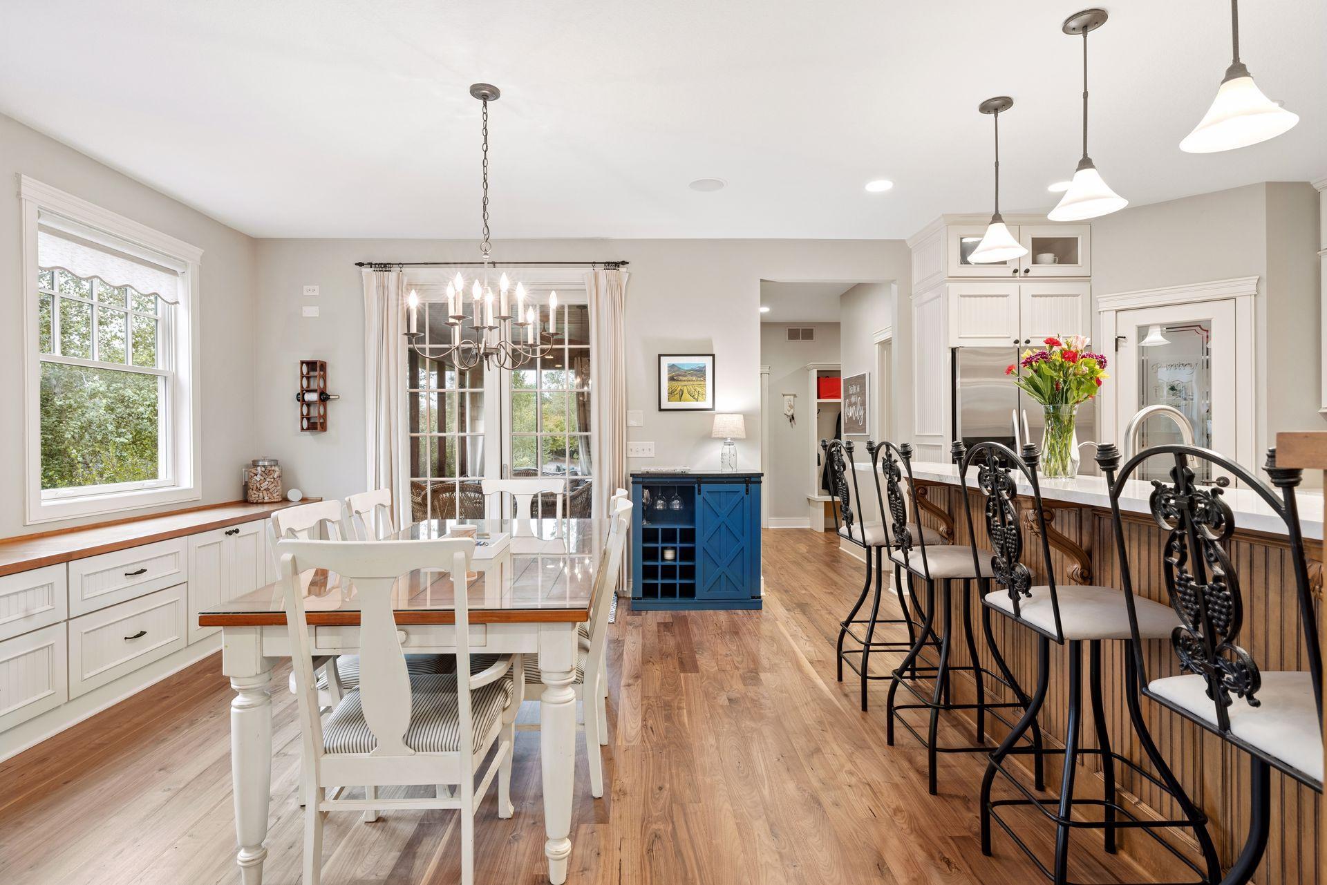 Dining area with a white table, chandelier, and kitchen island lined with black metal stools.