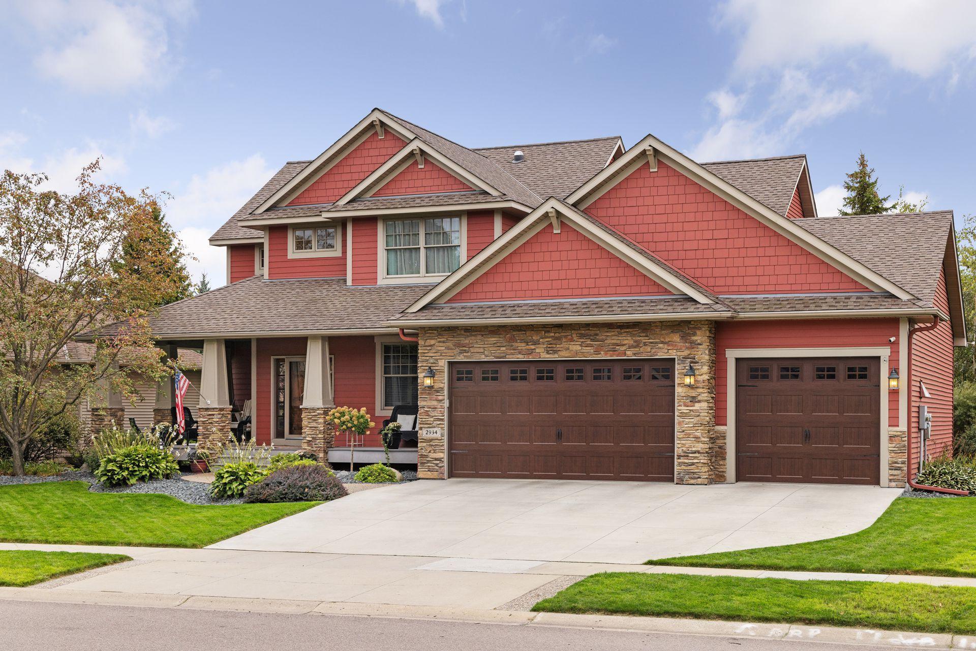 Red two-story home with stone accents, a covered porch, and two garage doors.