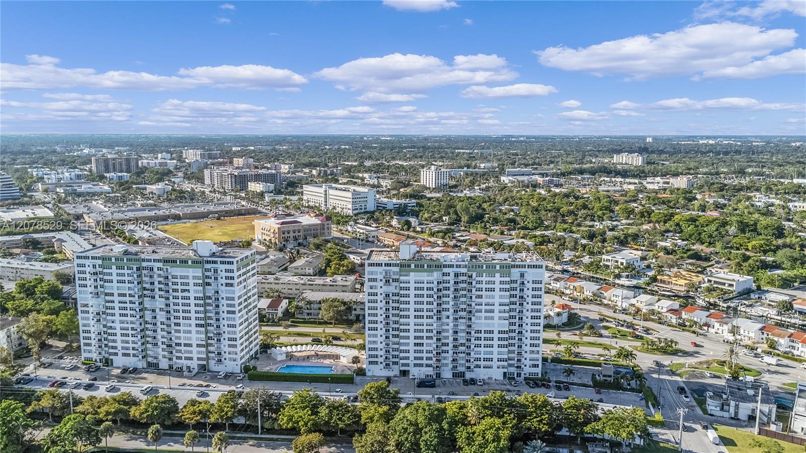 Aerial view of two white condominium towers, with a swimming pool and North Miami cityscape.