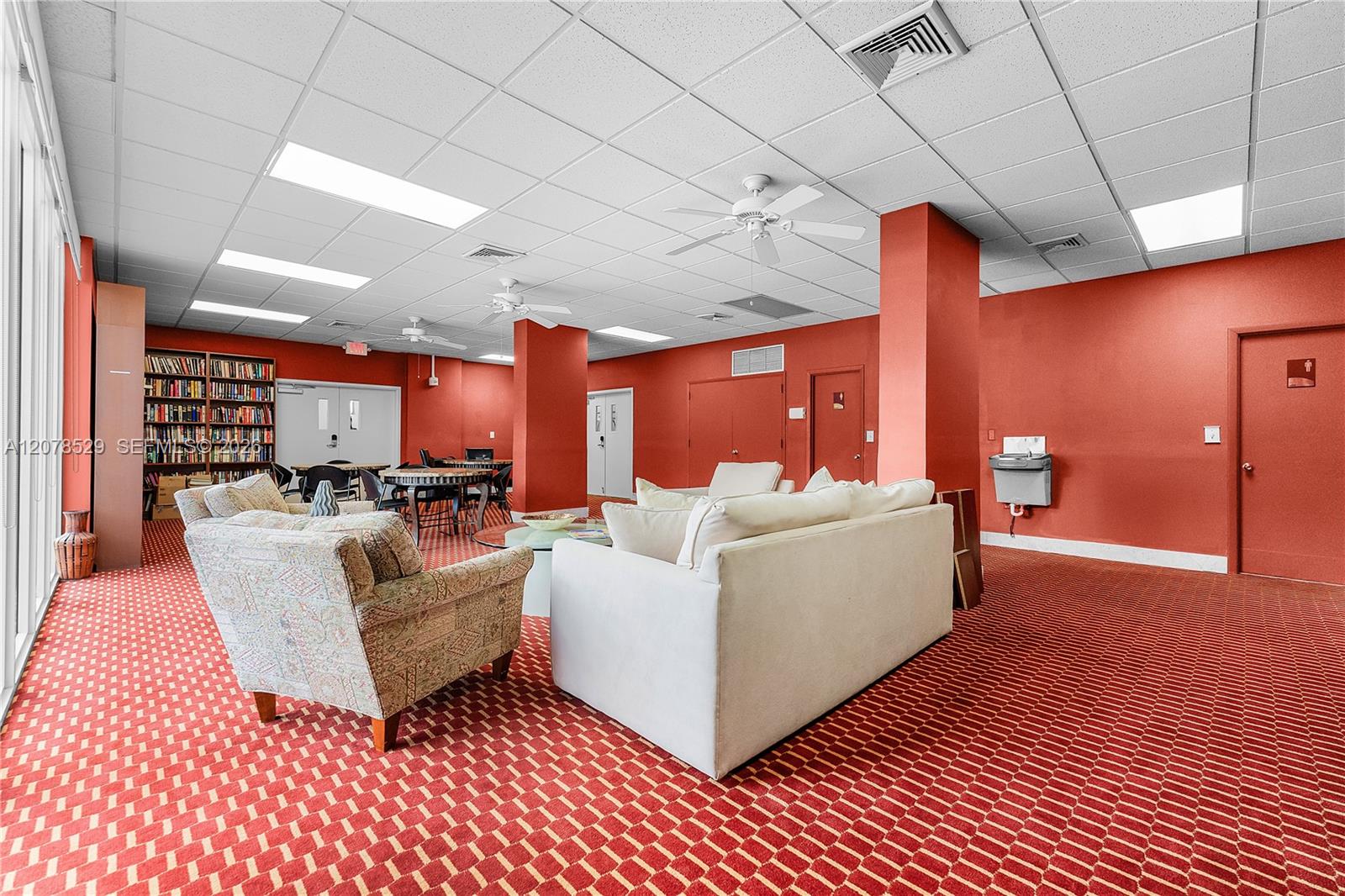 Furnished condominium lounge with sofas, a bookcase, red walls, and patterned carpet.