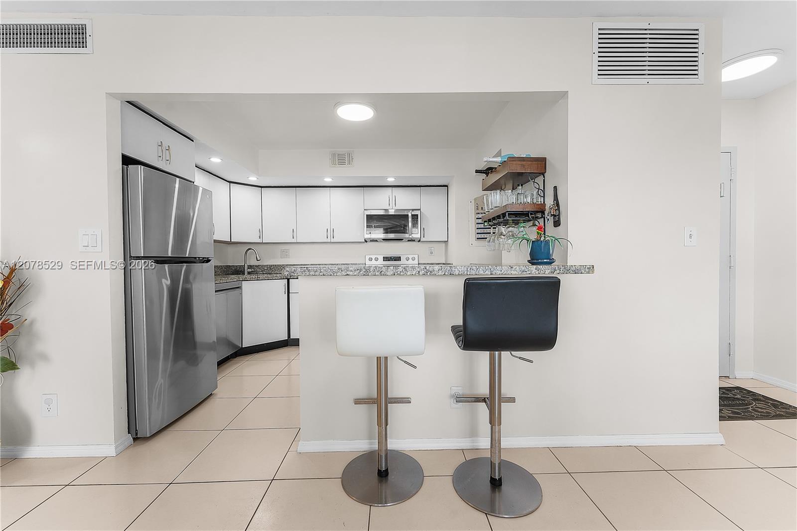 Condo kitchen with white cabinets, stainless steel appliances, and a granite breakfast bar with two stools.