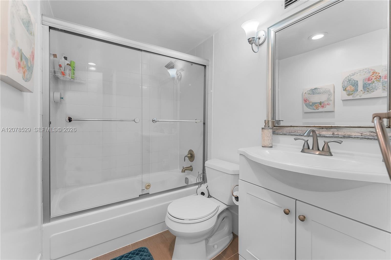 Bathroom with a glass-enclosed tub, white vanity, and floral wall art.