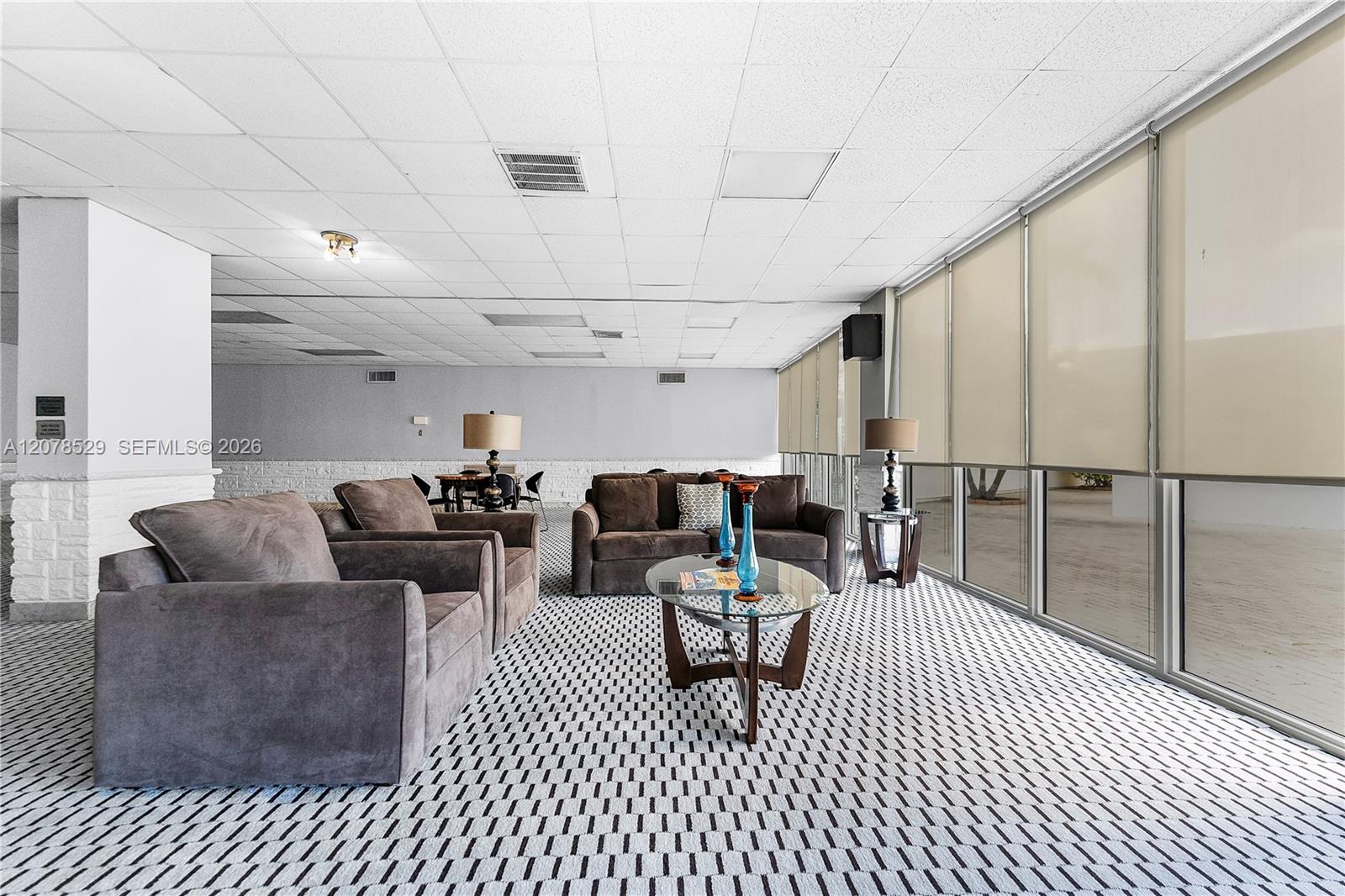 Furnished condo lounge with gray sofas, a glass coffee table, and floor-to-ceiling windows.