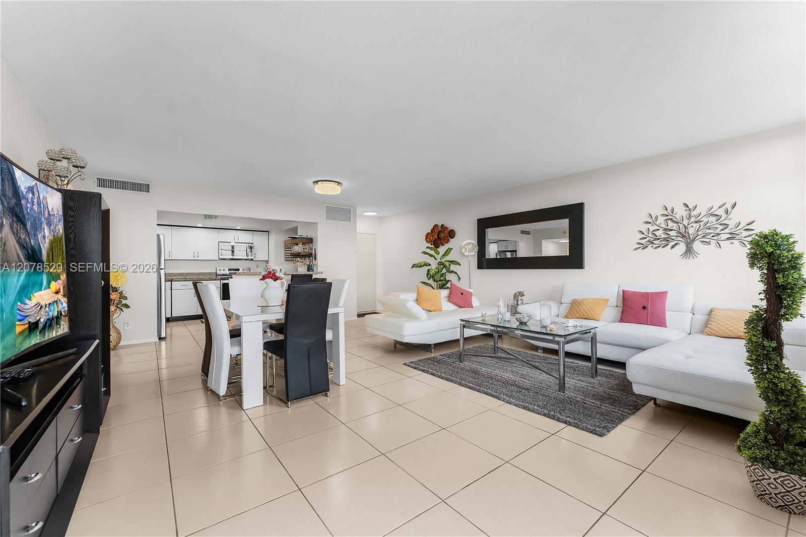 Furnished condo living and dining area with a white sectional, glass coffee table, and open kitchen.