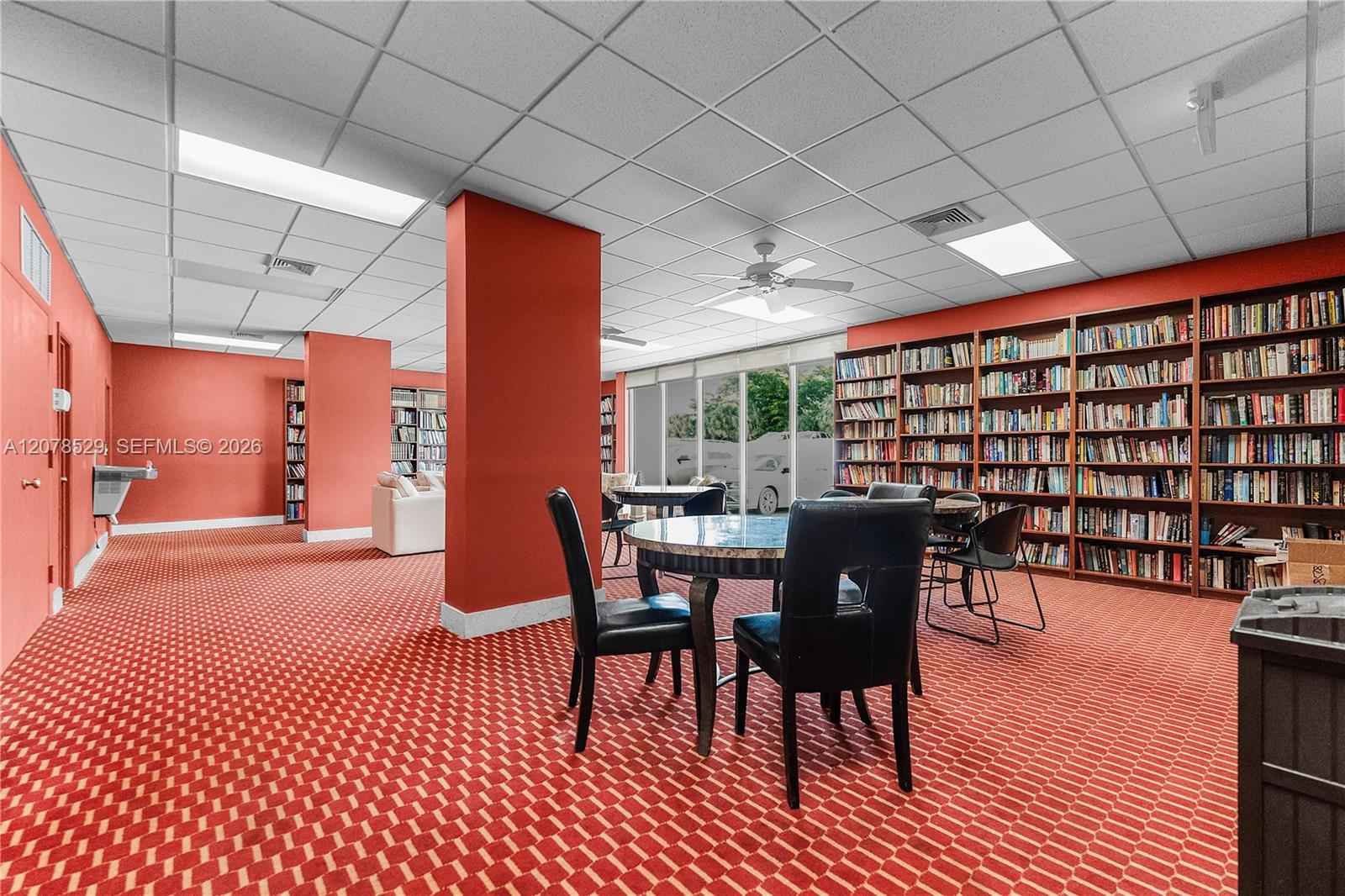 Community library with extensive bookshelves, round tables, and red patterned carpet.