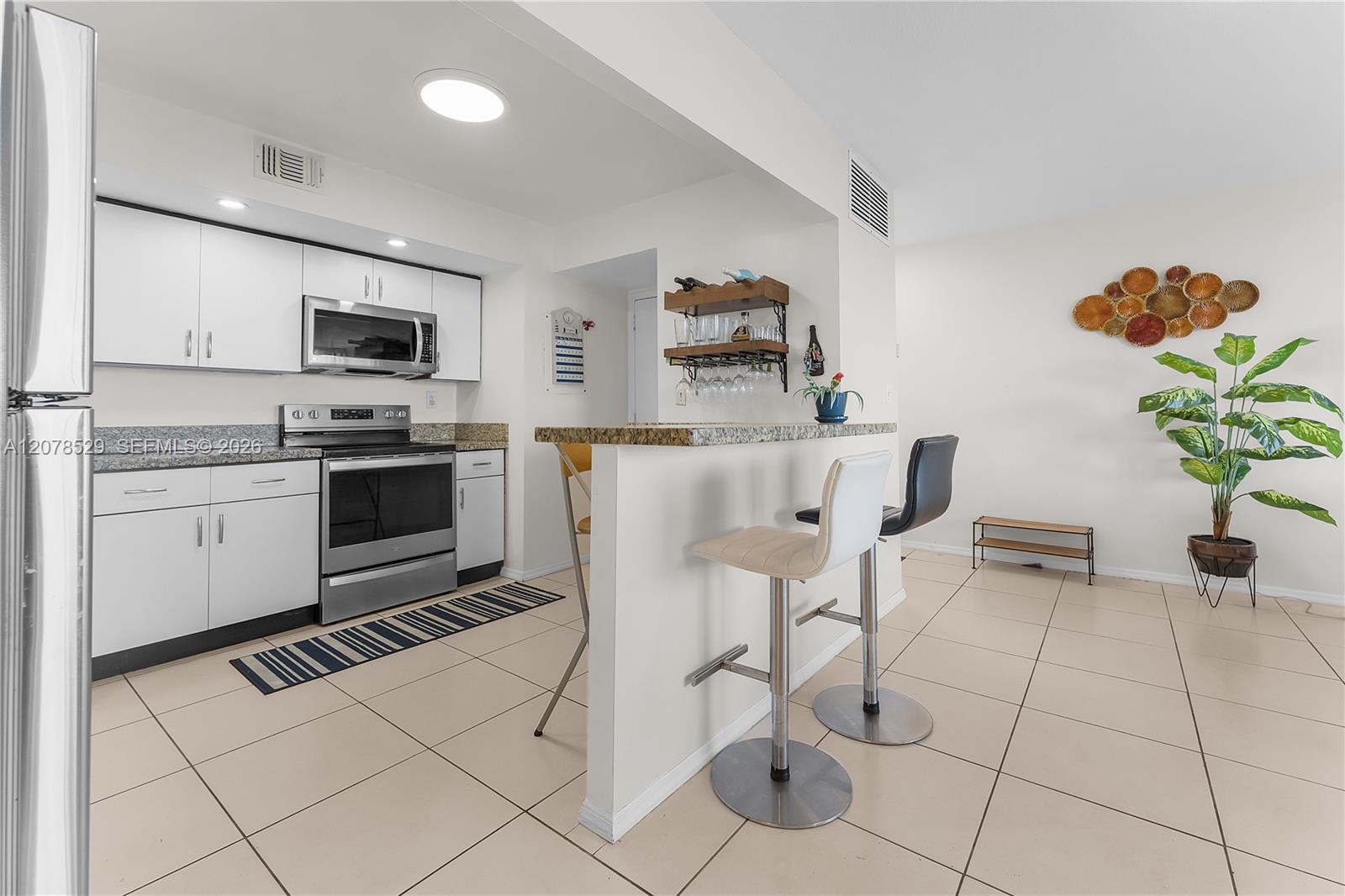 Condo kitchen with white cabinets, stainless steel appliances, granite breakfast bar, and two stools.