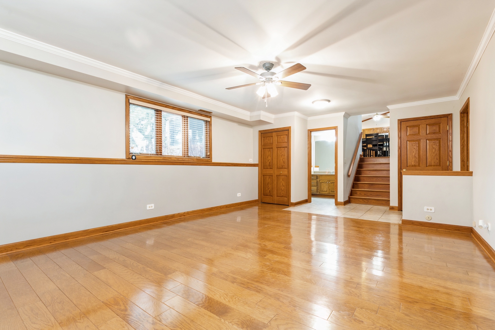Empty living room with polished hardwood floors, oak trim, and stairs to the upper level.