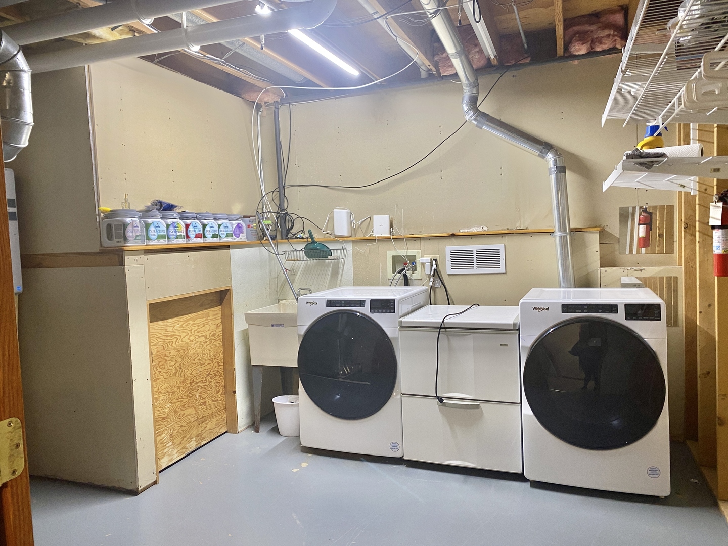 Basement laundry room with front-loading washer and dryer, utility sink, and exposed ceiling ductwork.