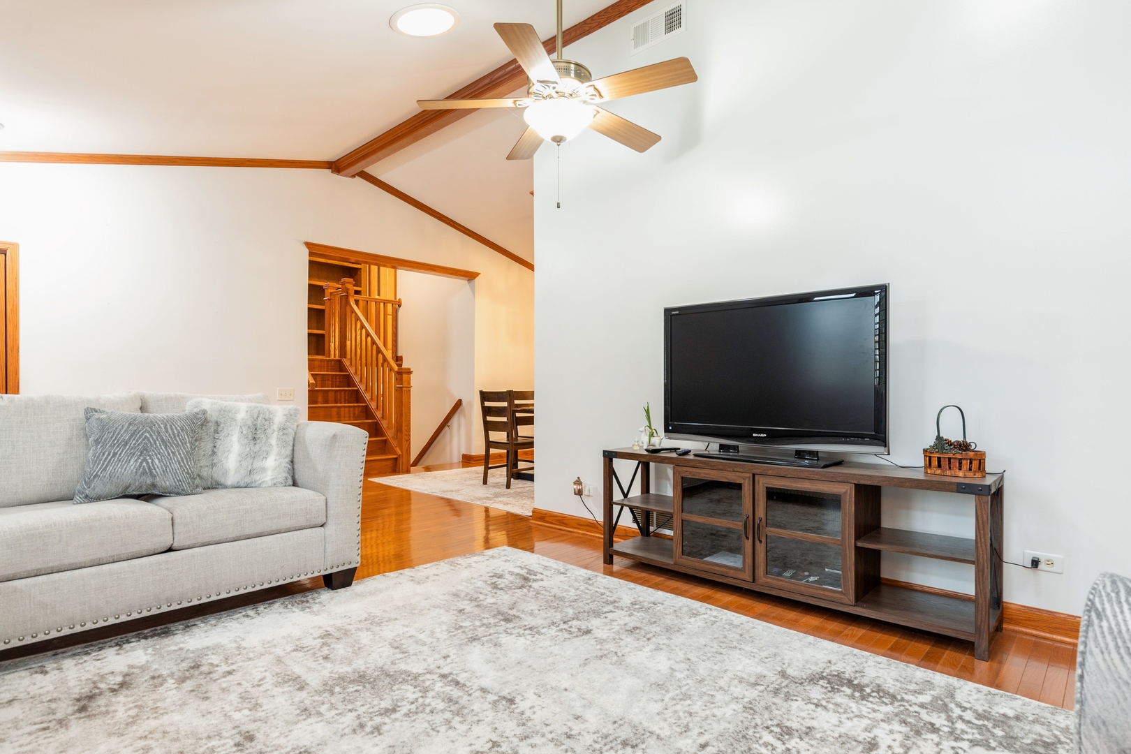 Living room with a gray sofa, hardwood floors, and a wood staircase beneath a vaulted ceiling.