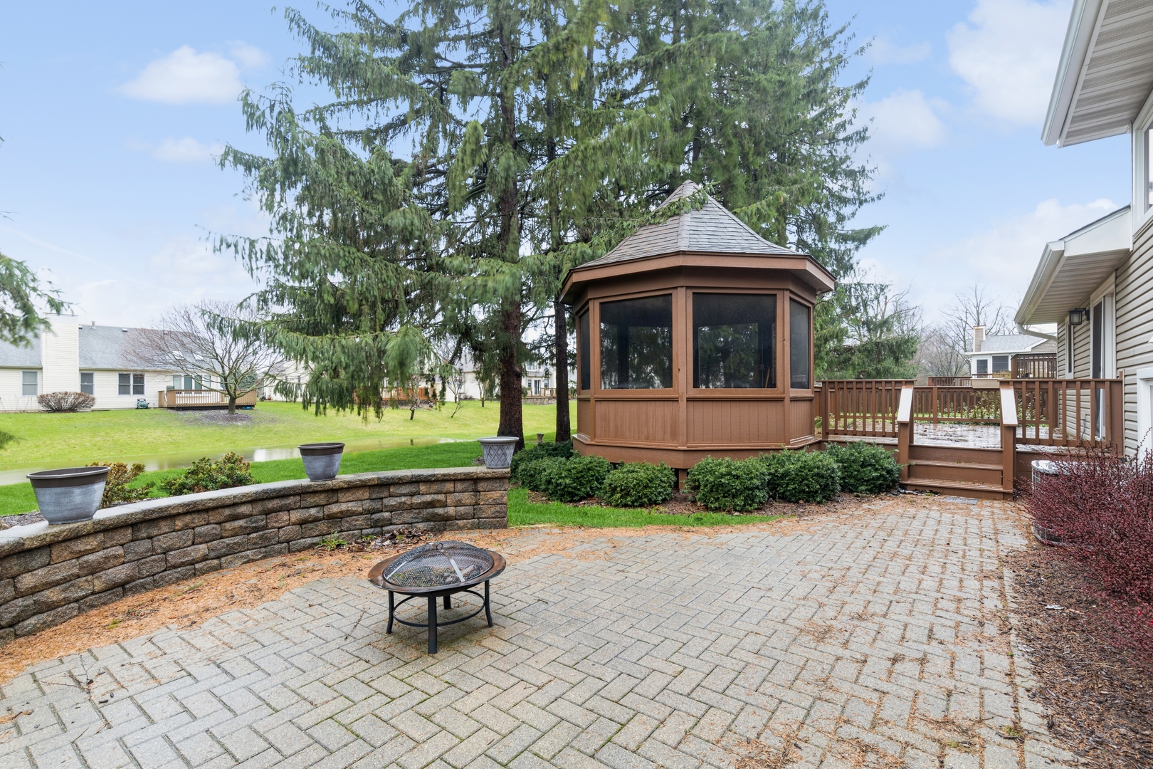 Backyard patio with an octagonal screened gazebo, raised deck, pavers, and a small pond.
