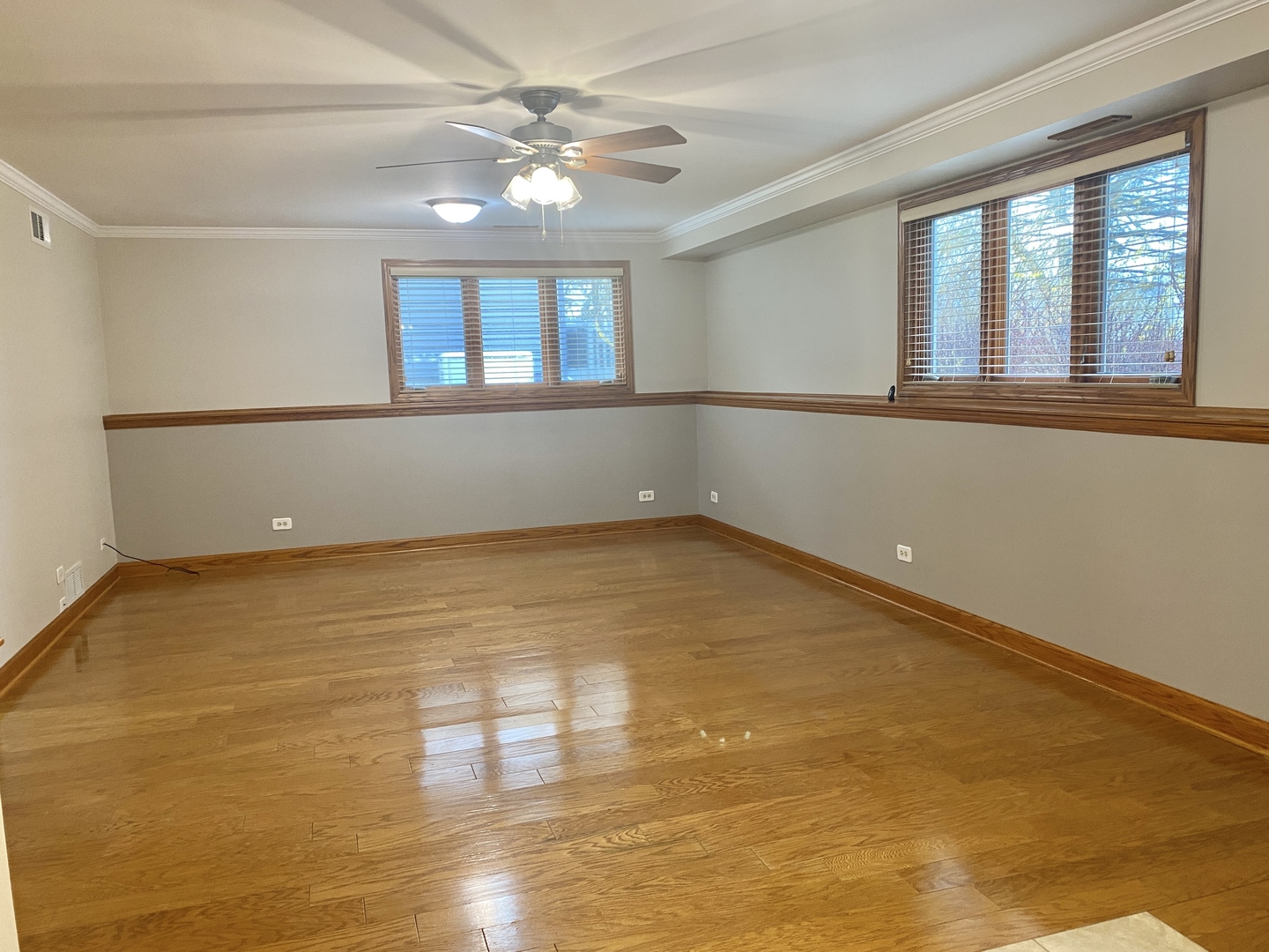 Empty room with hardwood floors, wood trim, two windows, and a ceiling fan.