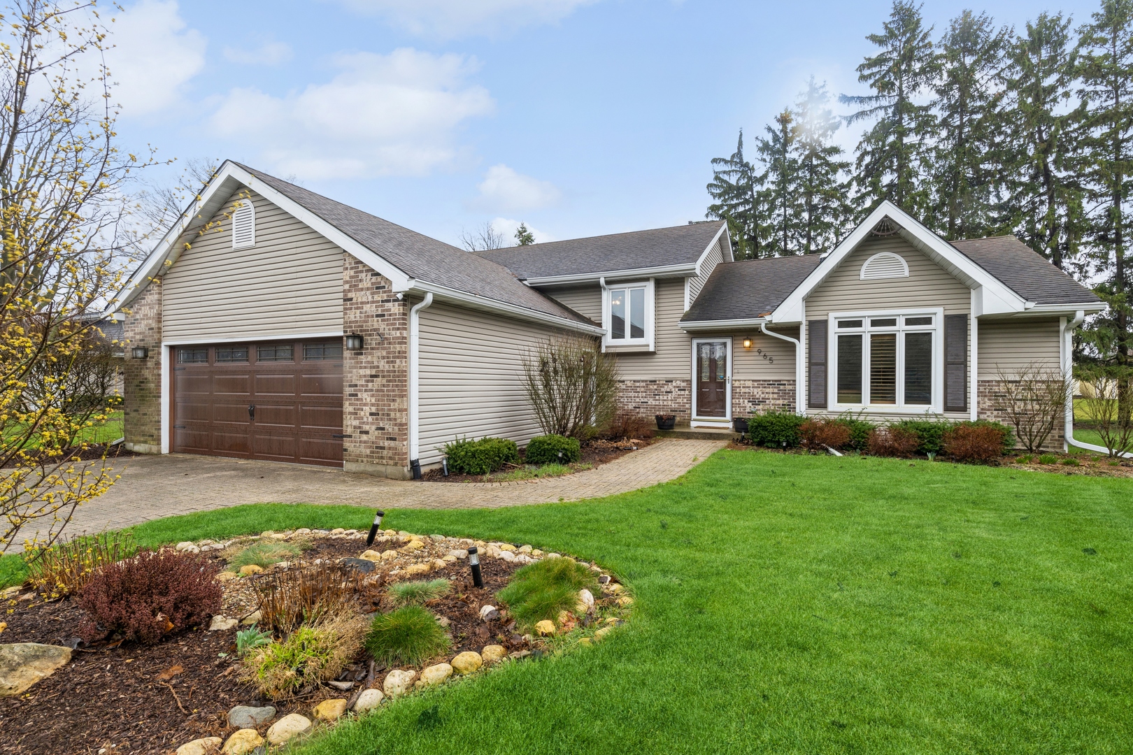 Single-story beige-and-brick home with a two-car garage, curved walkway, and landscaped front lawn.