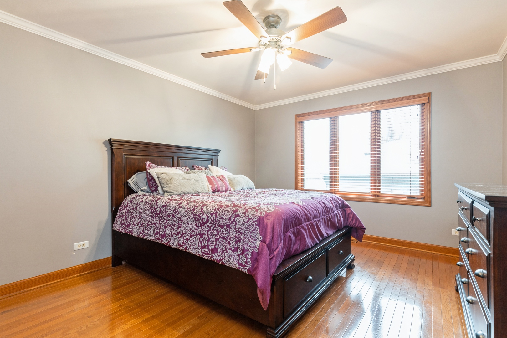 Bedroom with purple patterned bedding, dark wood furniture, hardwood floors, and a ceiling fan.