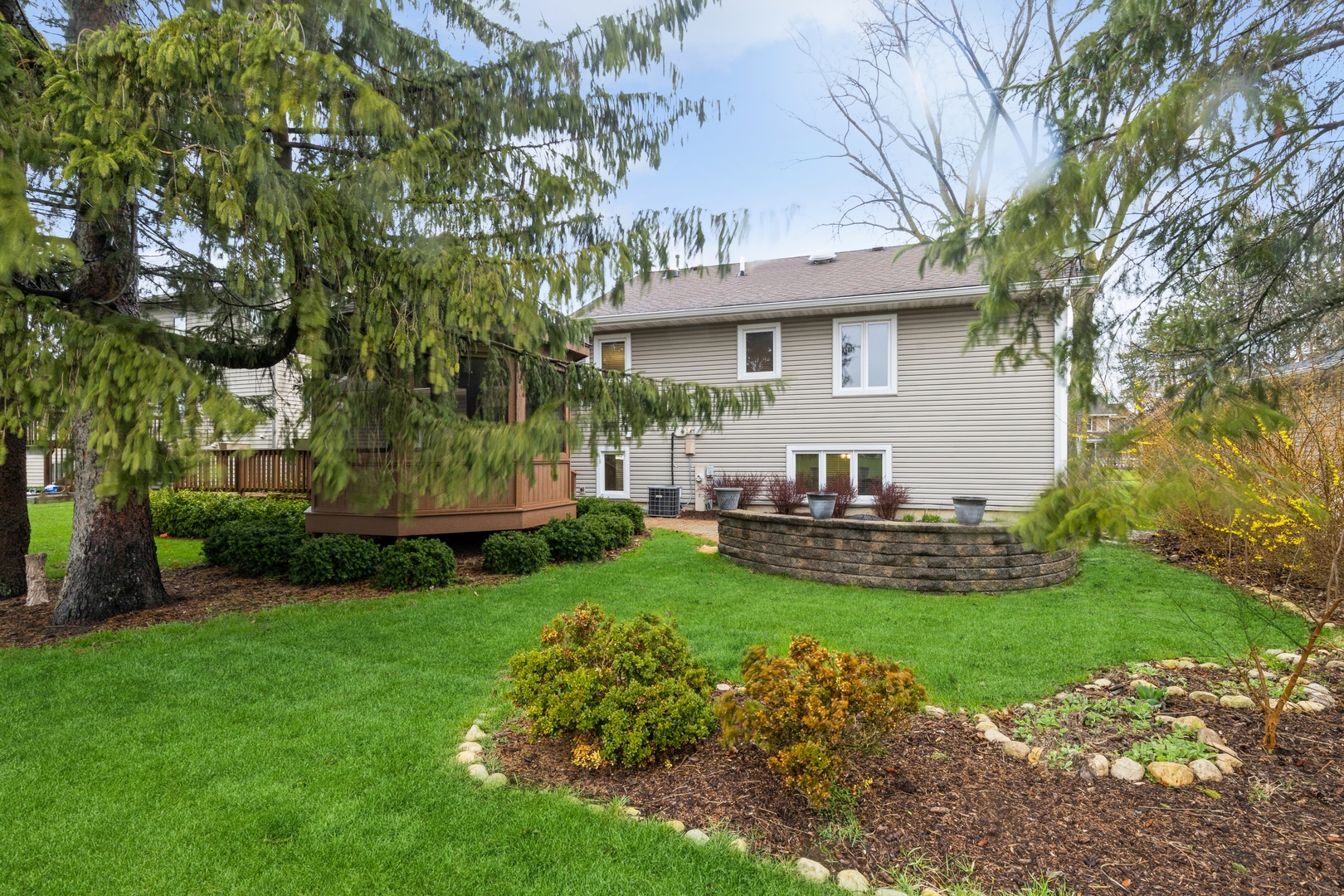 Rear exterior with a raised wooden deck, curved retaining wall, and landscaped lawn.