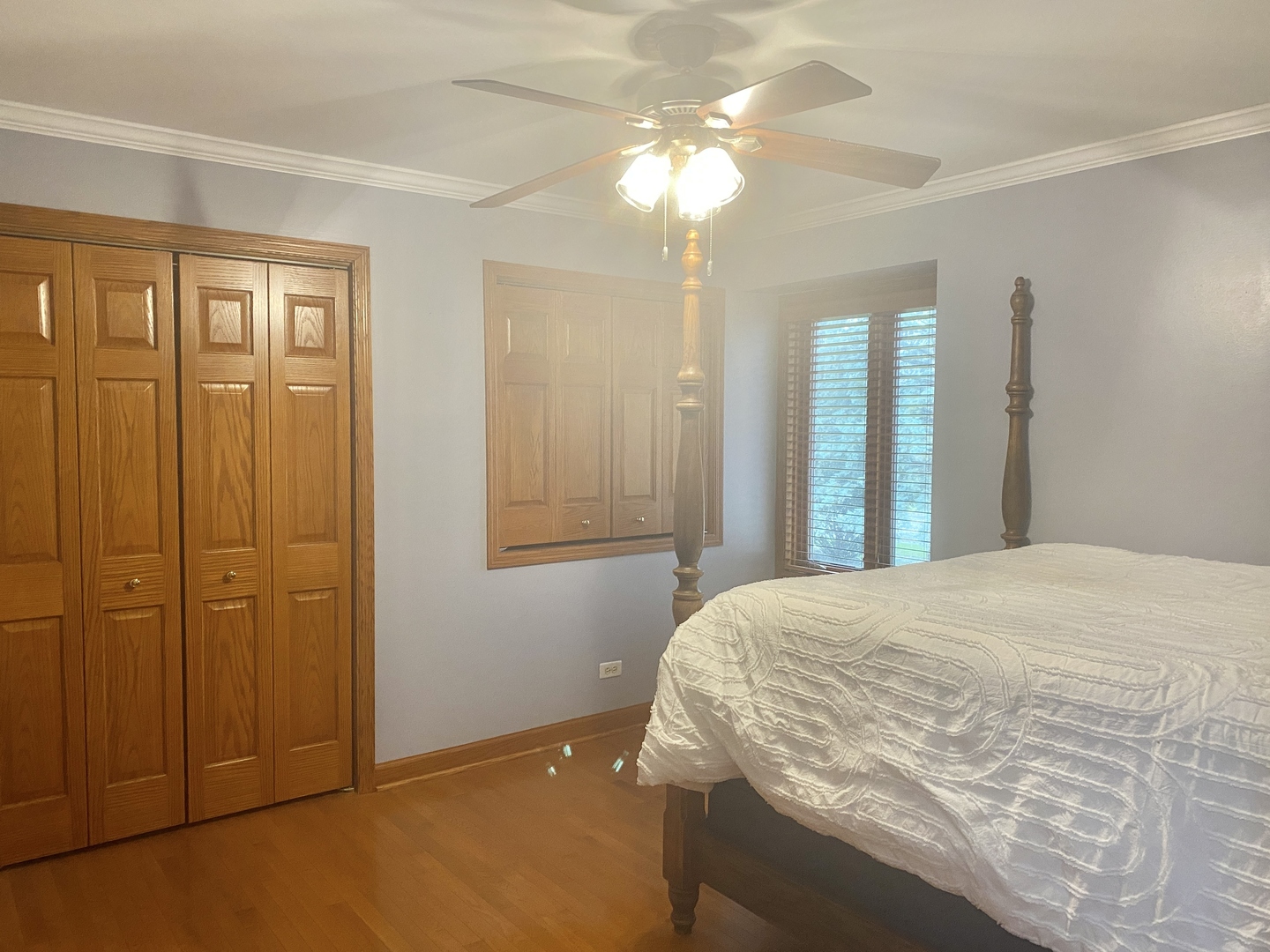 Bedroom with a white quilted bed, wood floors, paneled closet doors, and a ceiling fan.