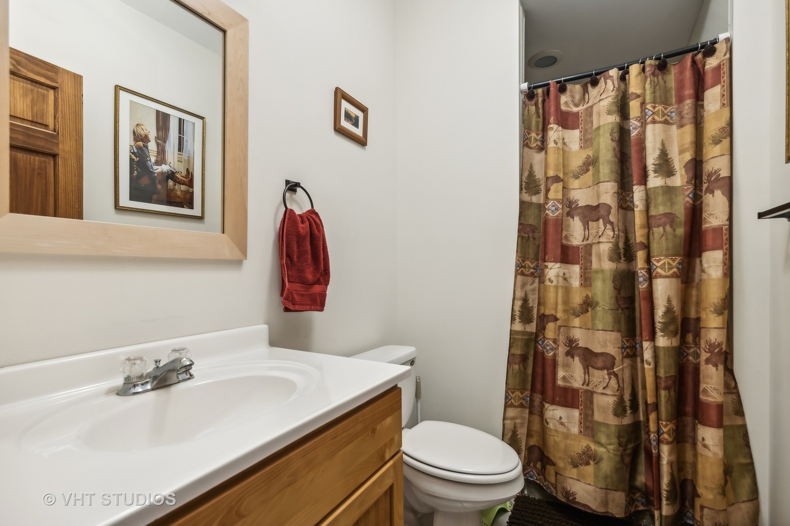 Bathroom with a wood vanity, white sink, toilet, and woodland-patterned shower curtain.