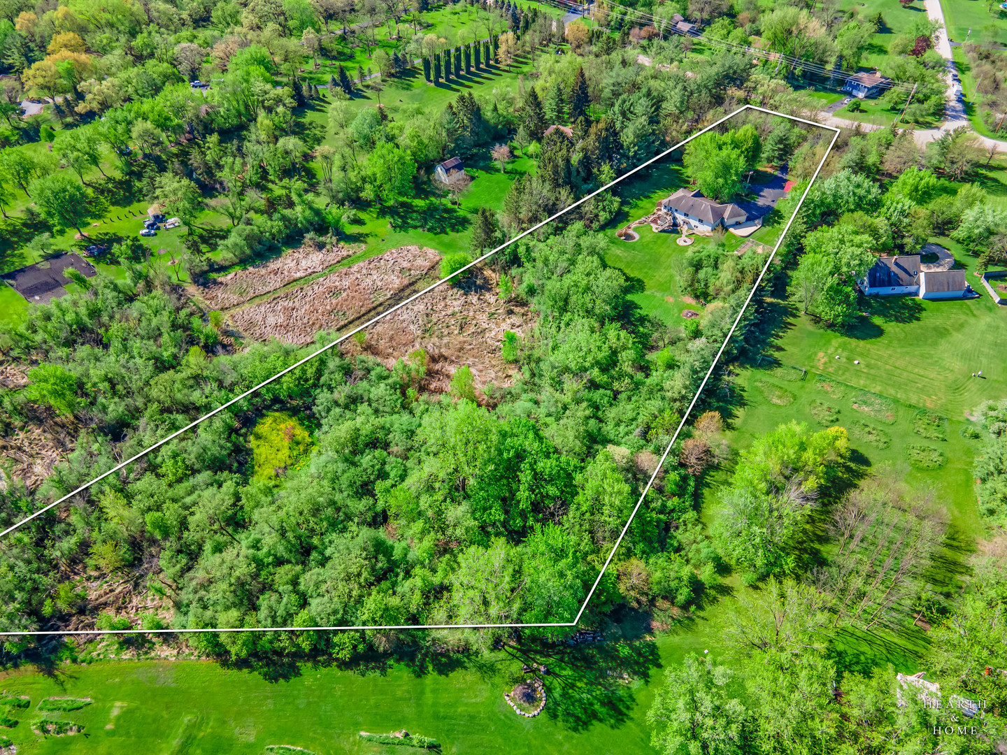 Aerial view of a home and wooded acreage outlined by a white property boundary.