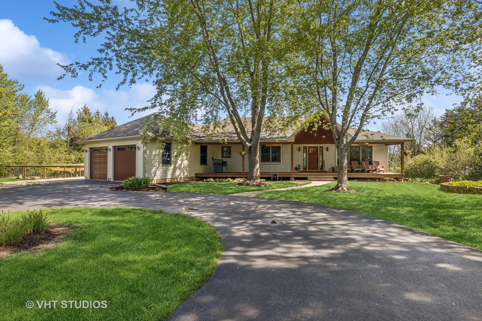Single-story home with a two-car garage, covered porch, mature trees, and curved driveway.