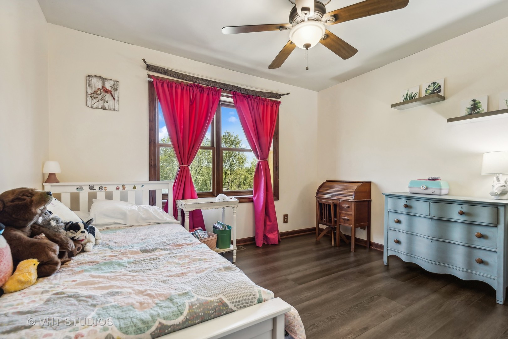 Bedroom with a white bed, bright red curtains, ceiling fan, and dark wood flooring.