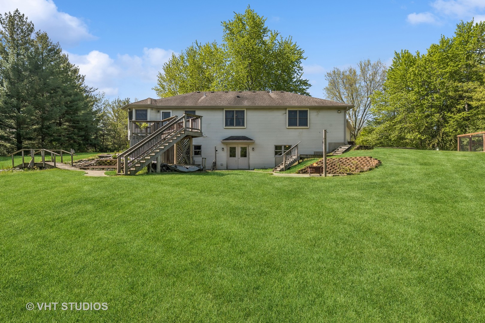 Rear of a two-story house with a raised deck and stairs overlooking a broad lawn.