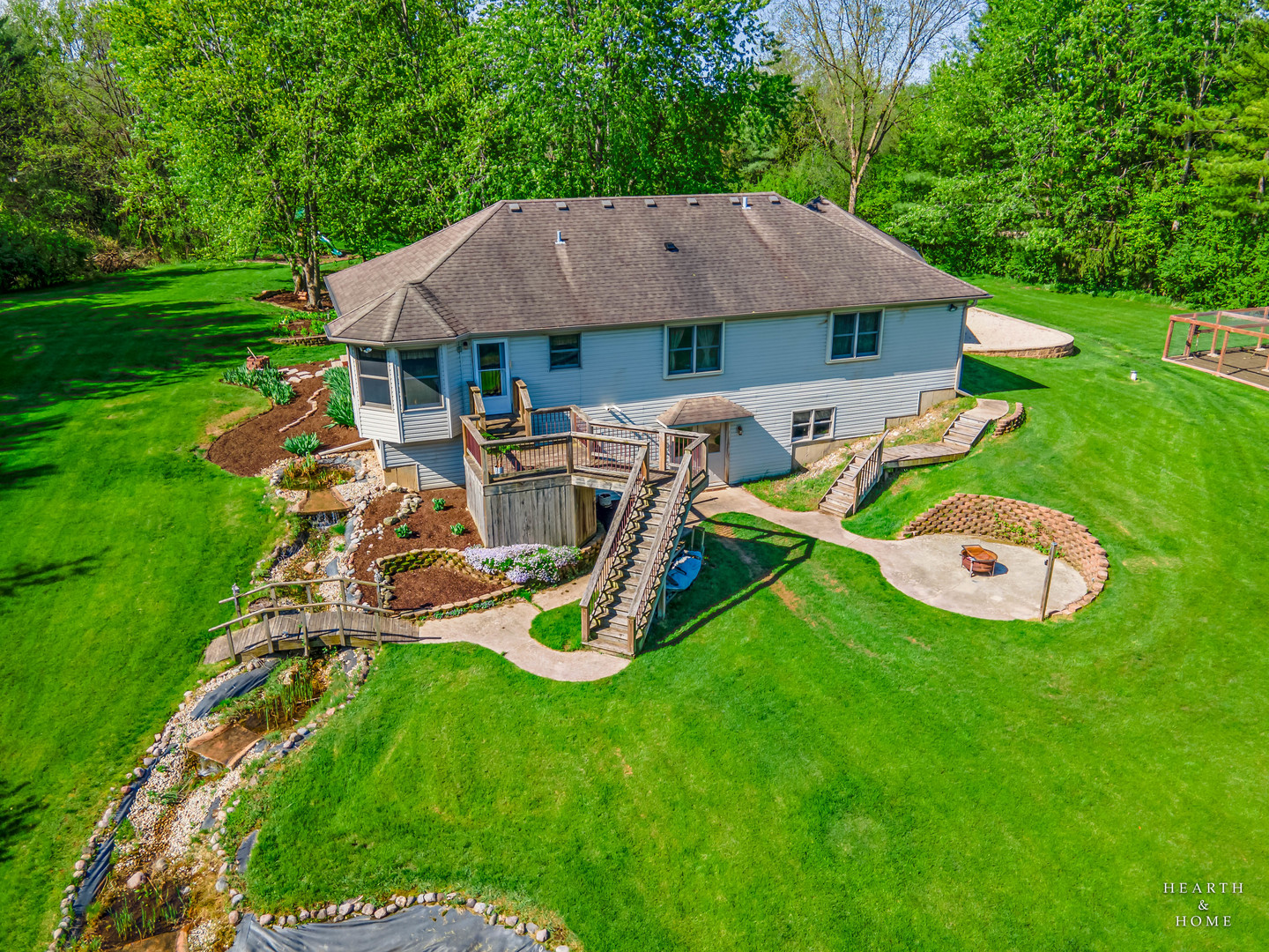 Rear of a house with a raised deck, landscaped stream, broad lawn, and circular fire-pit patio.