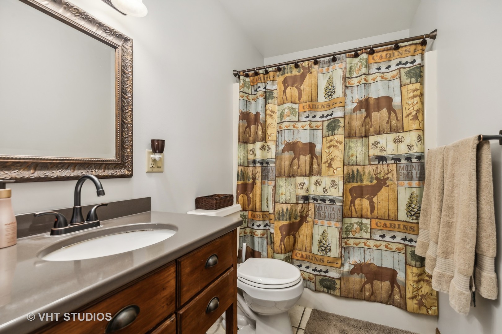Bathroom with a dark wood vanity, oval sink, and woodland-print shower curtain.